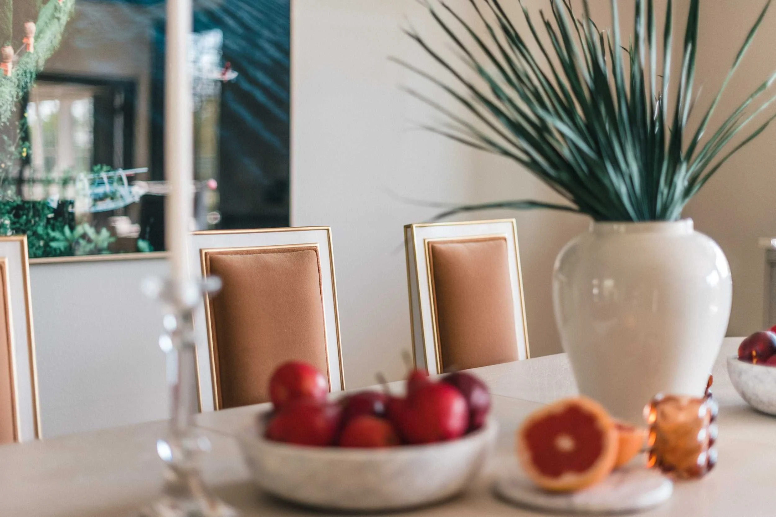 Close-up of the high-backed dining chairs that feature a white wooden frame paired with tan/camel leather upholstery.