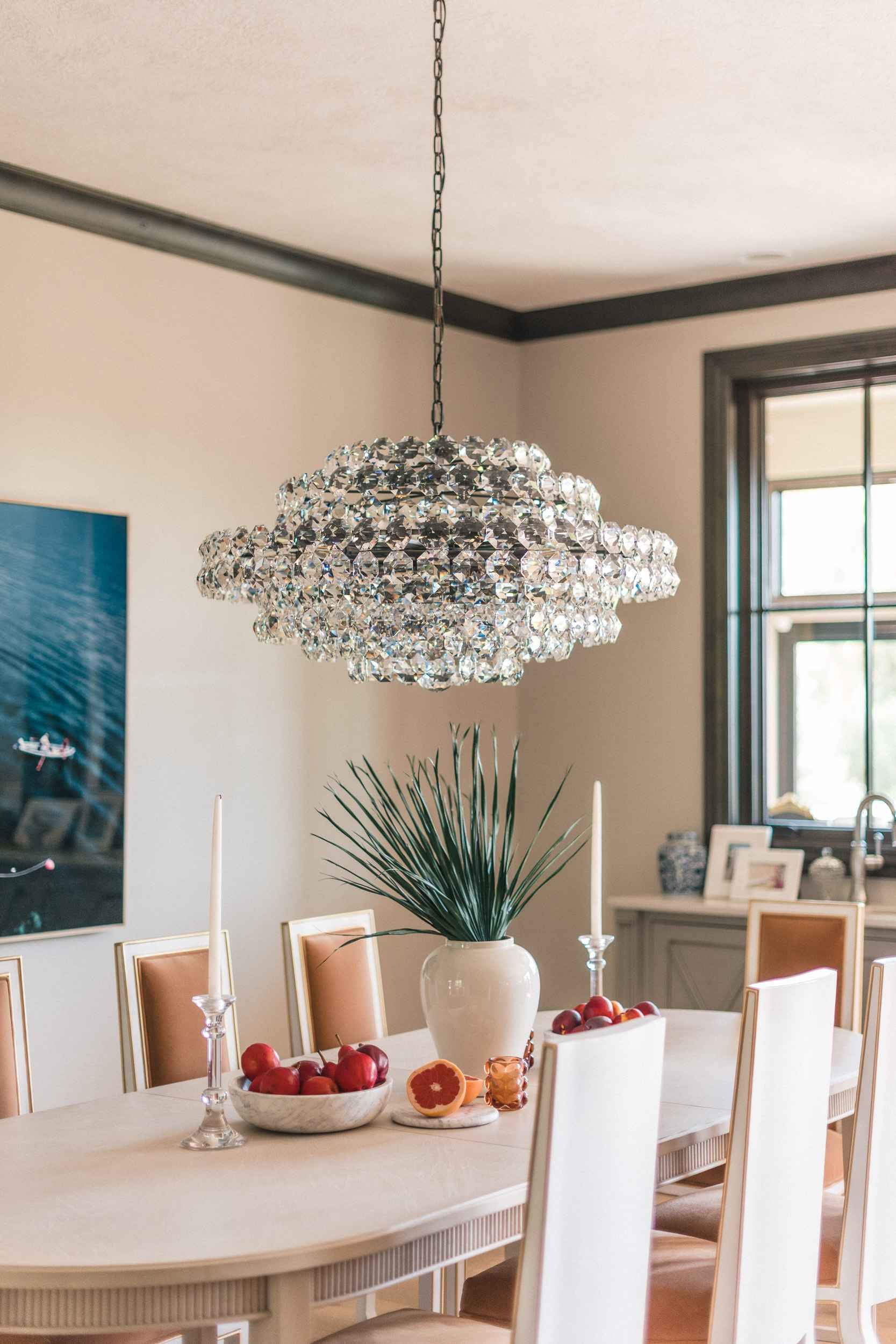 View of the cloud-shaped crystal chandelier hanging over the dining table, with the white vase and fruit in the foreground.