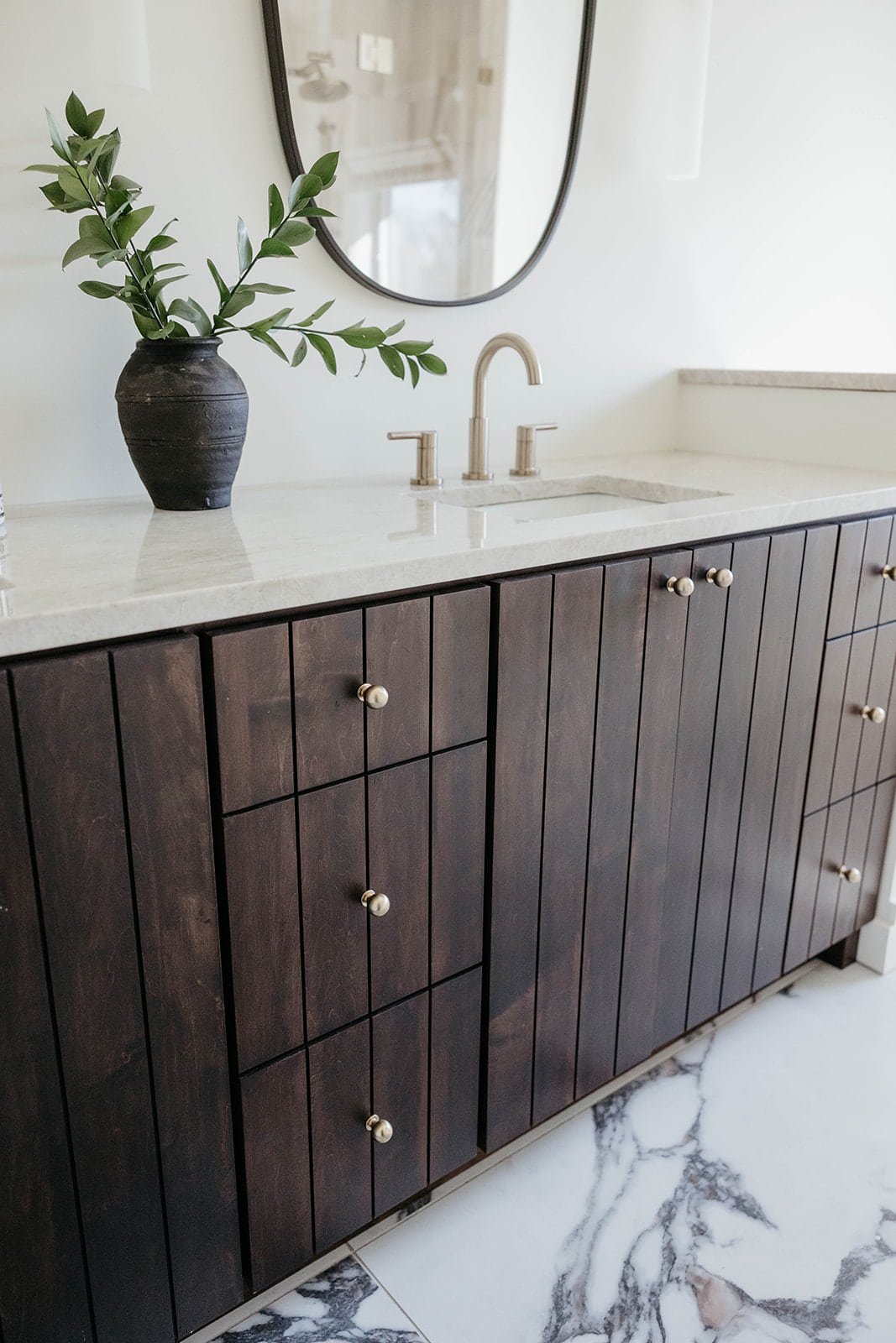 Close-up of the dark-stained wood vanity with a light countertop and round brass knobs. The vanity sits on the heavily veined marble floor.