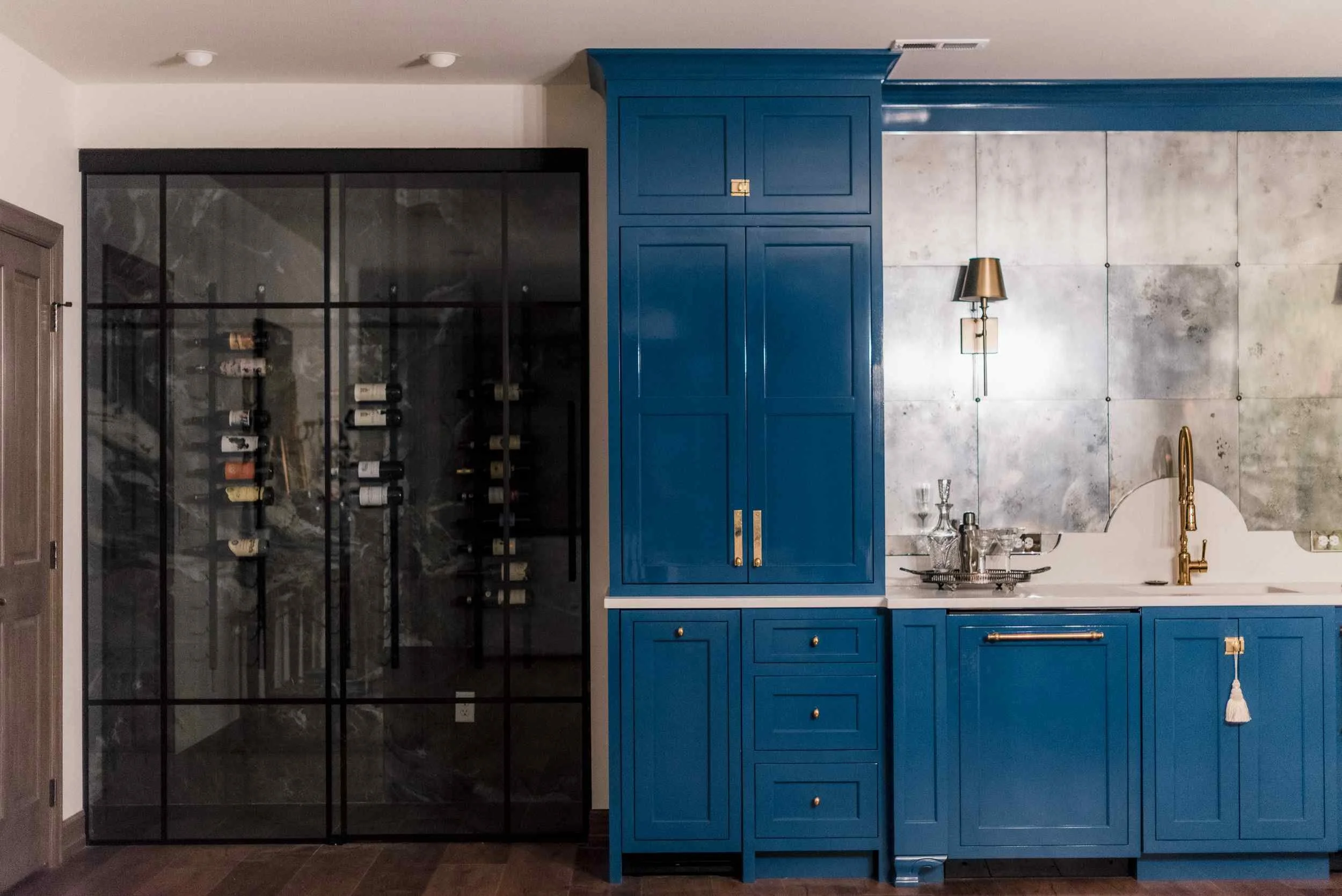 Home bar showing the blue cabinetry and a large, black-framed glass wall on the left, revealing a climate-controlled wine cellar.