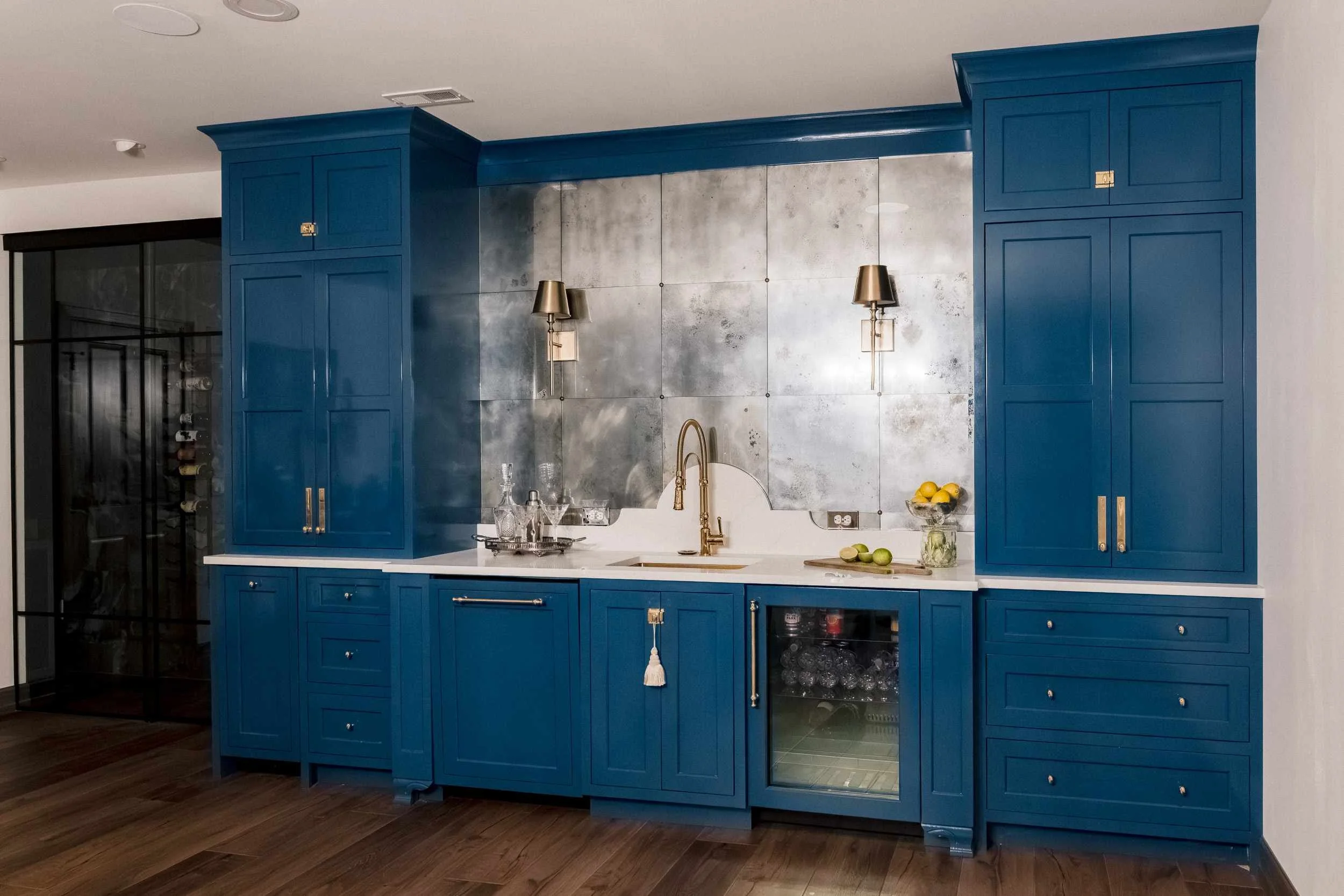Luxurious home bar with high-gloss cobalt blue cabinetry, white quartz countertop, and a distressed antique metal backsplash.