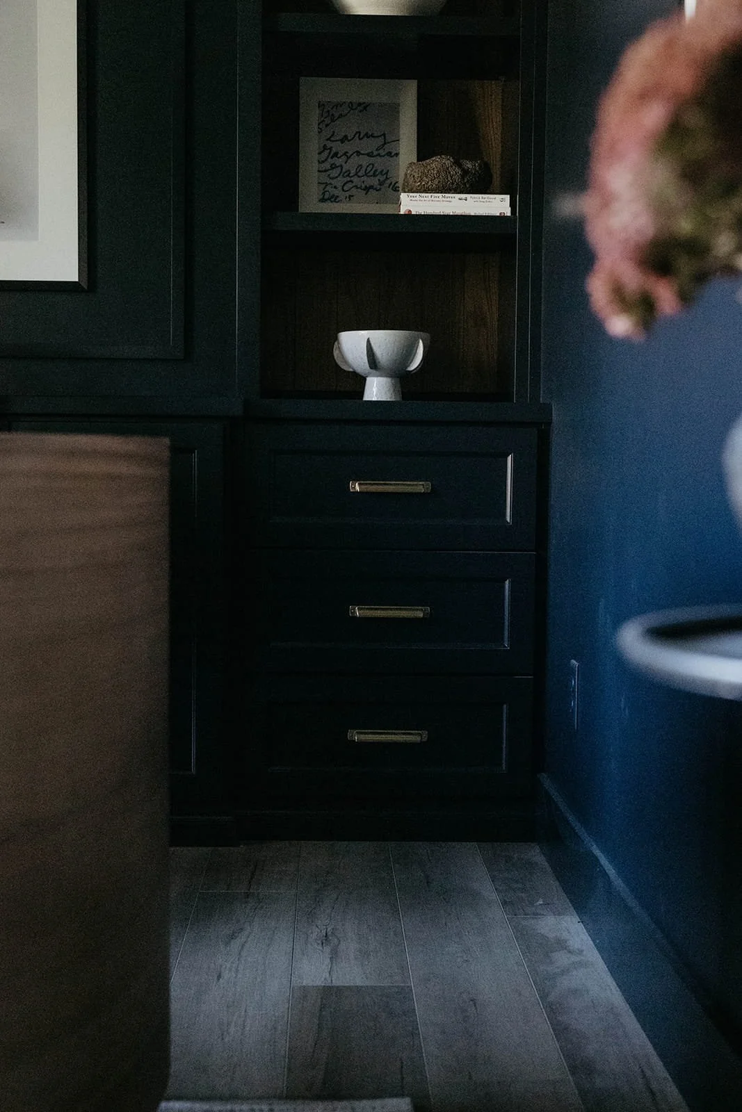 Close-up of dark built-in office cabinetry with three drawers and a white bowl accessory in an open niche, showcasing a masculine and moody design.