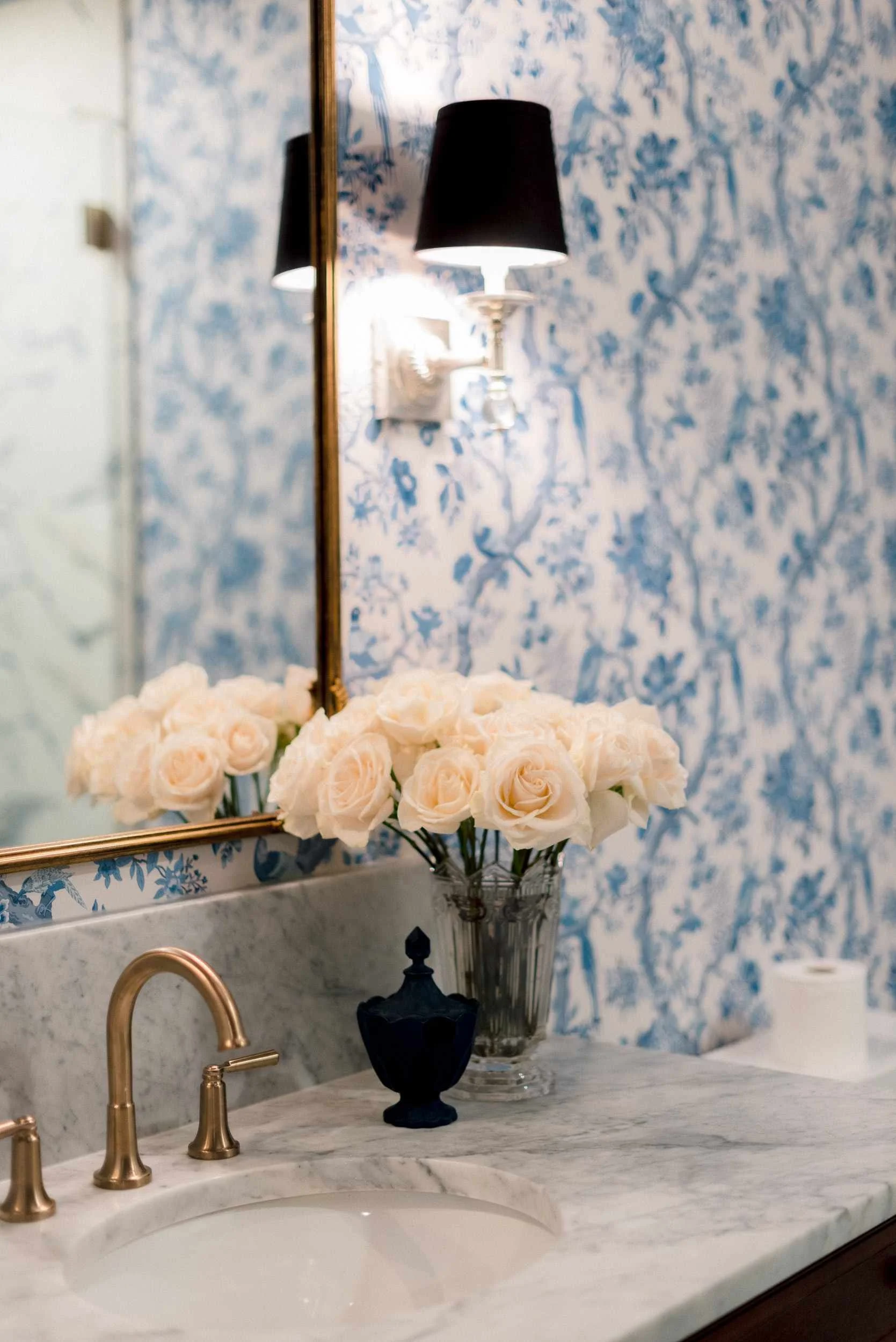 Close-up of the vanity sink and countertop, with the brass faucet, vase of roses, and the reflection of the gilt mirror.