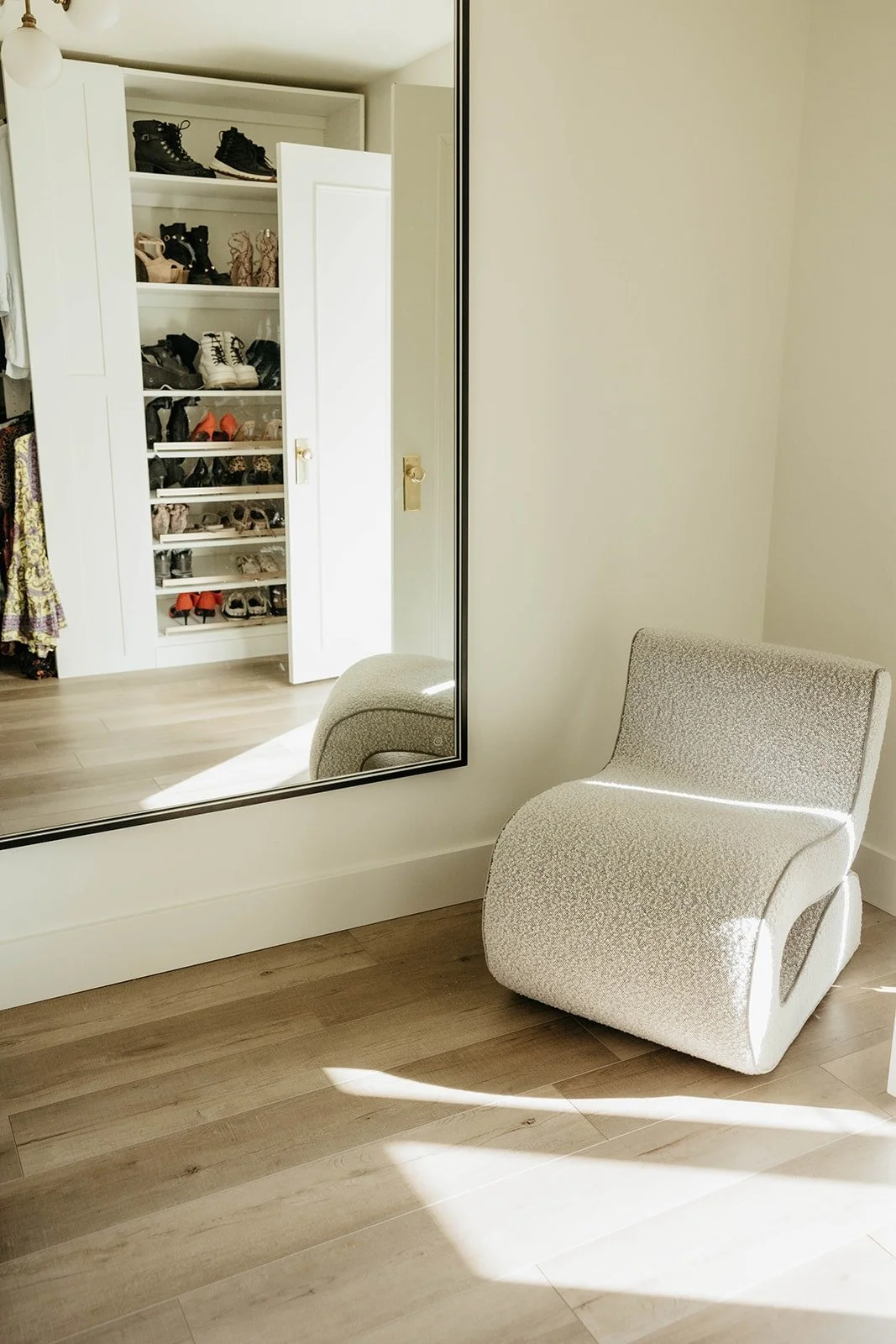 Sculptural accent chair and full-length mirror with a reflection of hidden shoe storage cabinet in the corner of the room. 