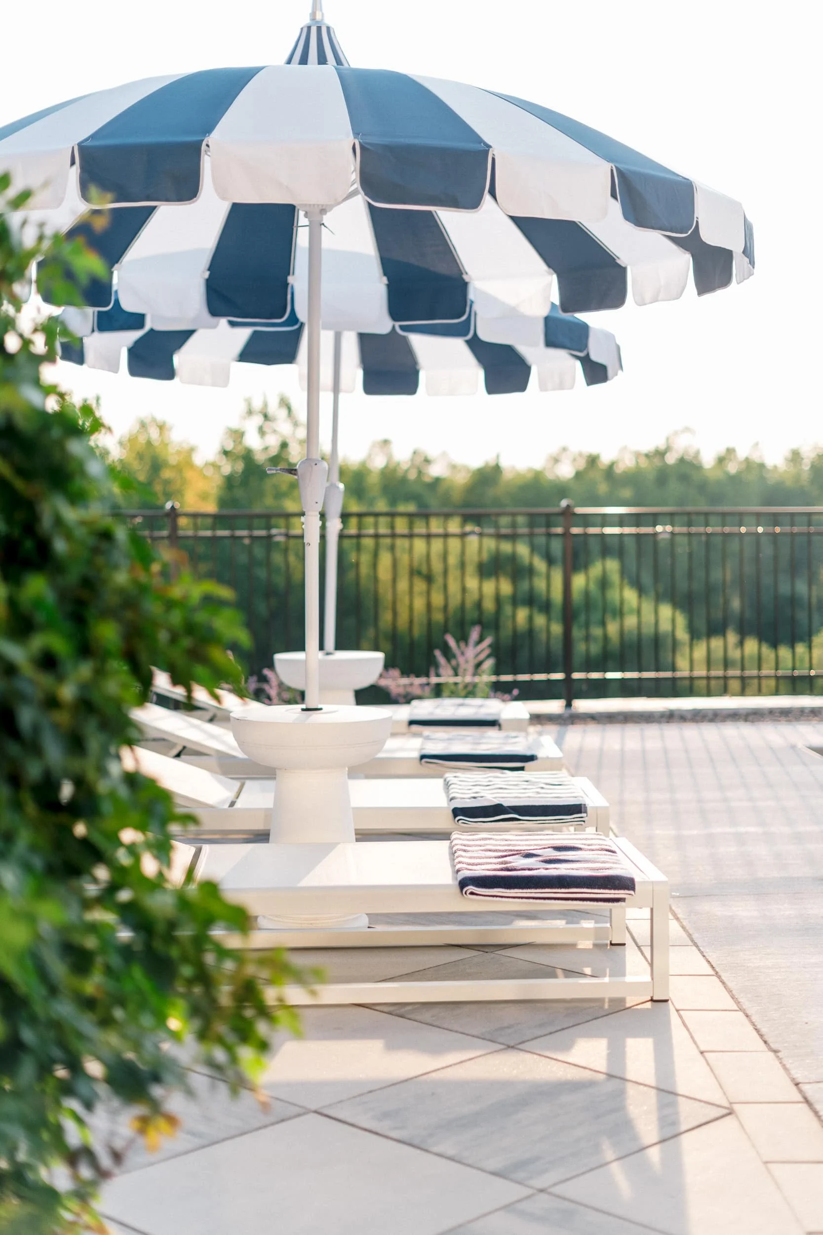 Bright, focused shot of a navy and white striped umbrella shading a white chaise lounge and side table on the patio.