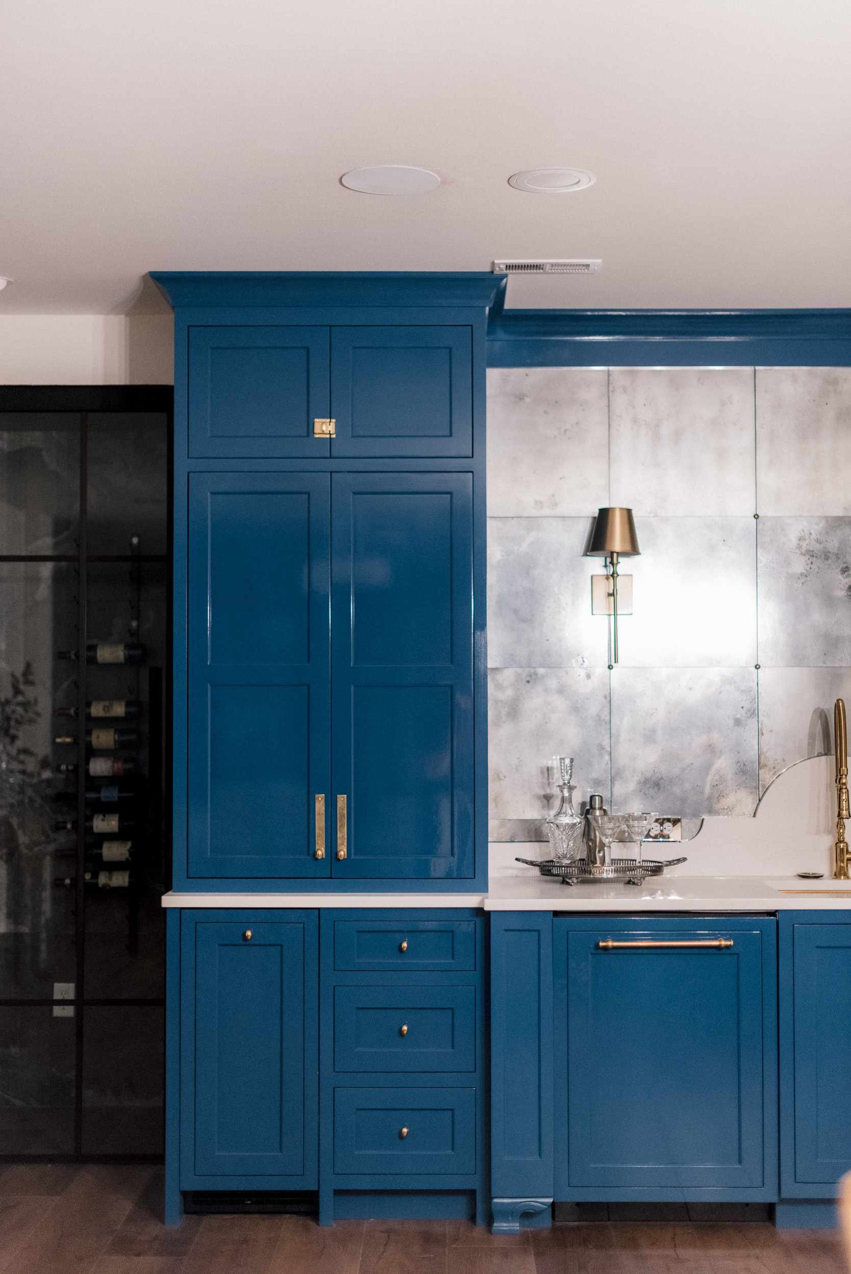 Wide view of the blue bar cabinetry, showing the integrated wine fridge, gold fixtures, and the antique metal backdrop.