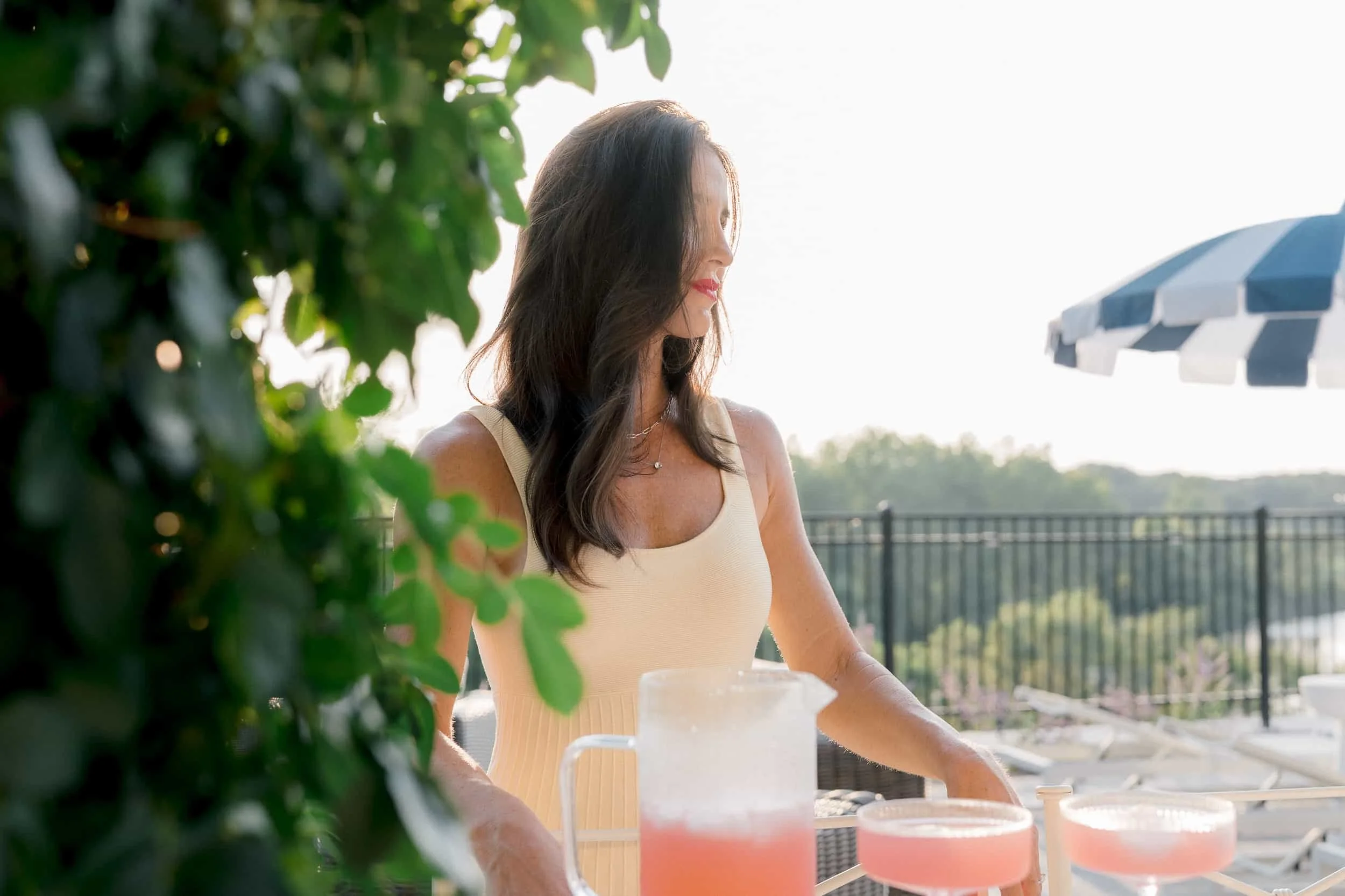 Christy Steen serving pink drinks at an outdoor setting with black iron fencing and greenery, a navy and white striped umbrella visible in the background.