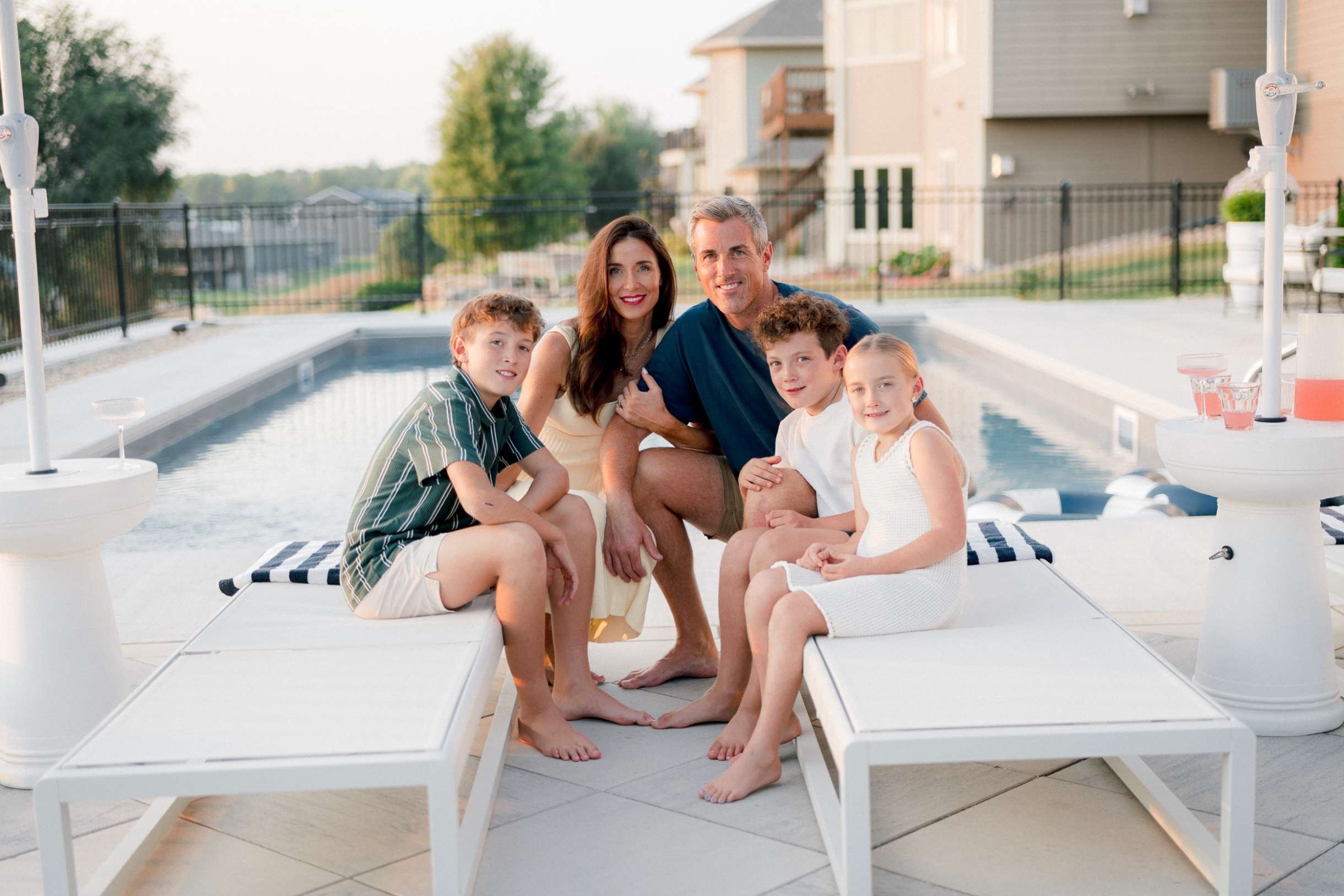 Christy Steen, husband, and three kids sitting and relaxing on the white outdoor daybeds near the swimming pool, with drinks nearby.