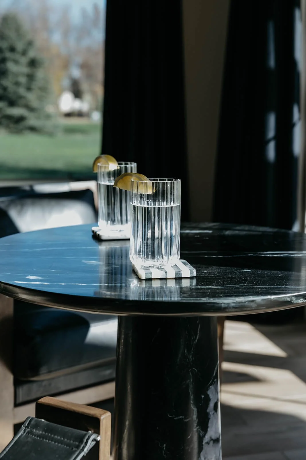 Tight close-up of a black marble-top side table with a sculptural base, holding two tall glasses of water with lemon slices, highlighting the outdoor view.