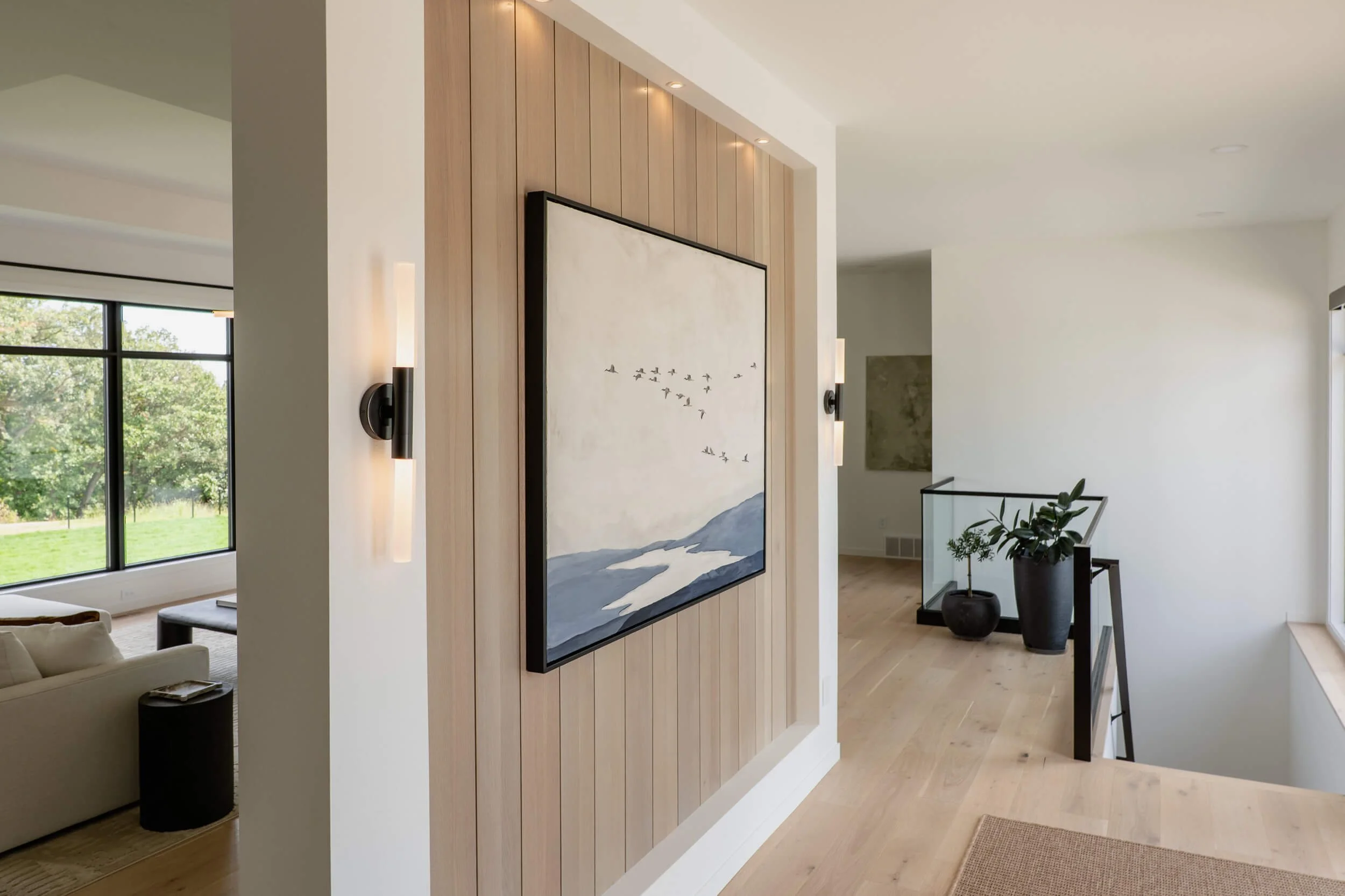 A modern entry area with light wood trim, vertical wood paneling, a piece of Christy Steen's original, abstract art, and vertical black sconces.