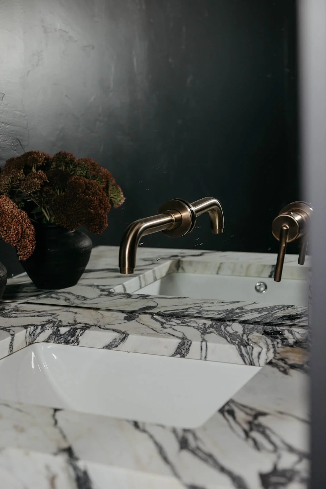 Close-up of the powder room vanity featuring a square white vessel sink, a brushed gold single-hole faucet, and a black vase with dried flowers on the marble counter.