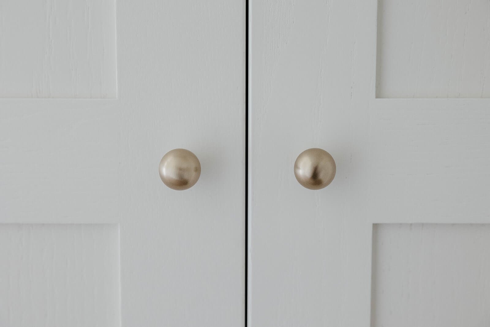 Close-up detail of two small, round brass door knobs on white paneled closet doors.