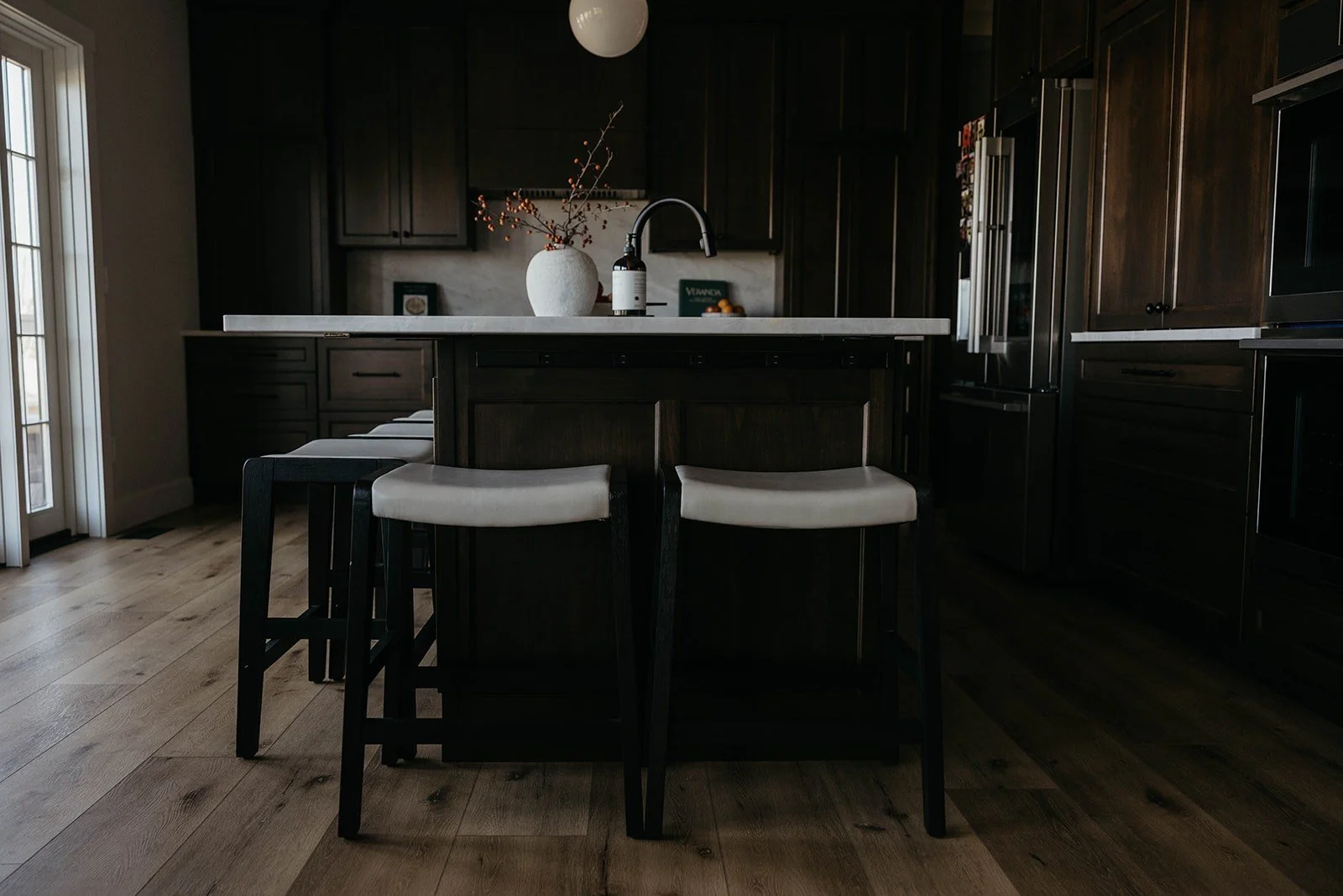 Close-up of the kitchen island with a white marble-look countertop, styled with a vase and fruit. Two dark counter stools are pulled up to the island.