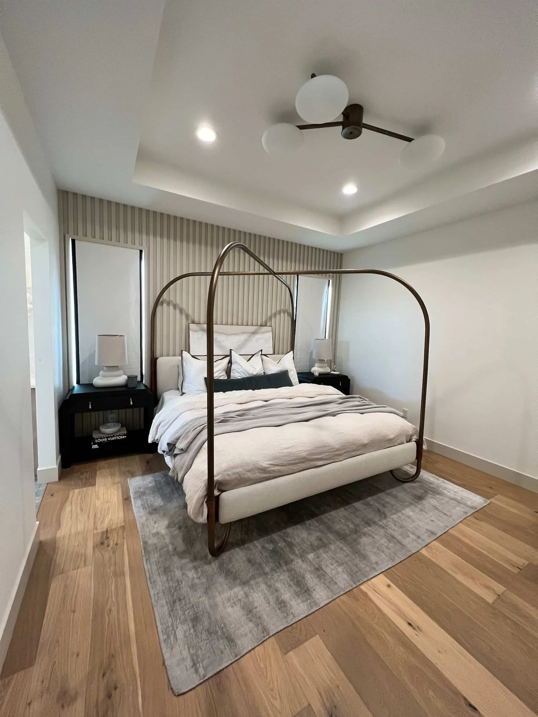 Master bedroom with a four-poster brass or gold canopy bed, dark nightstands, and a slatted wood accent wall behind the headboard.