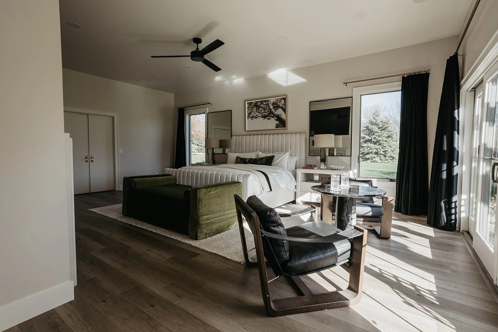 Wide view of the master bedroom with a dark accent wall, a green velvet accent sofa, and a large sliding glass door leading to an outdoor area.
