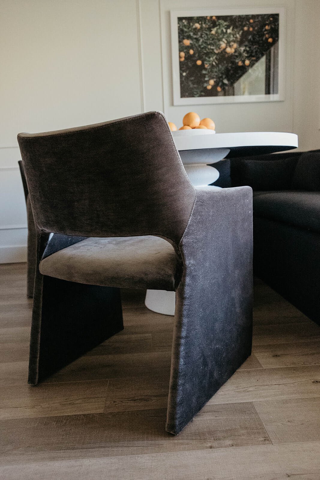 Close-up of a dramatic gray velvet dining chair with a sculpted base, part of a small breakfast nook with a built-in dark gray banquette.
