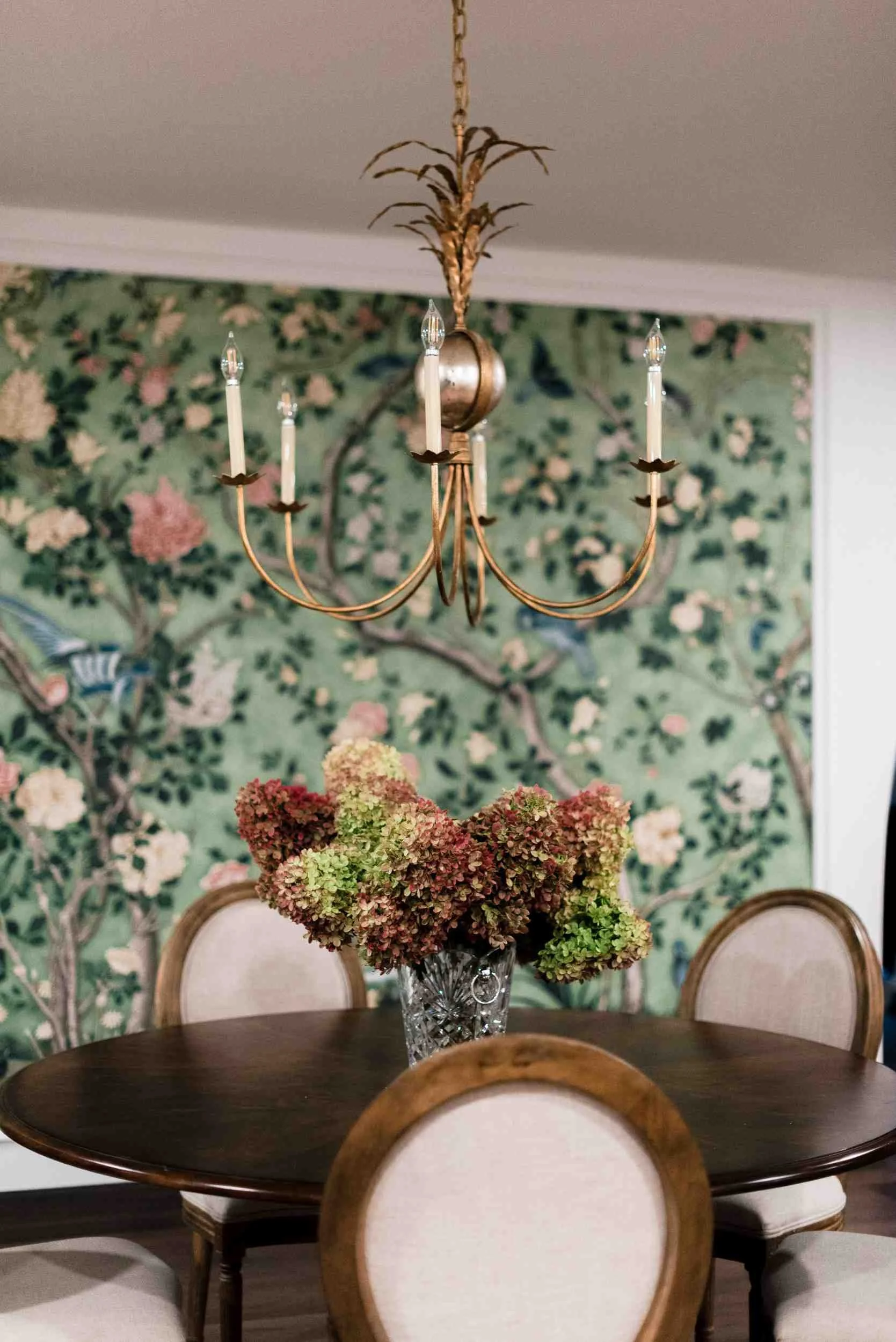 Close-up of the green chinoiserie wallpaper and a vintage brass chandelier with taper candles, above a round dining table.