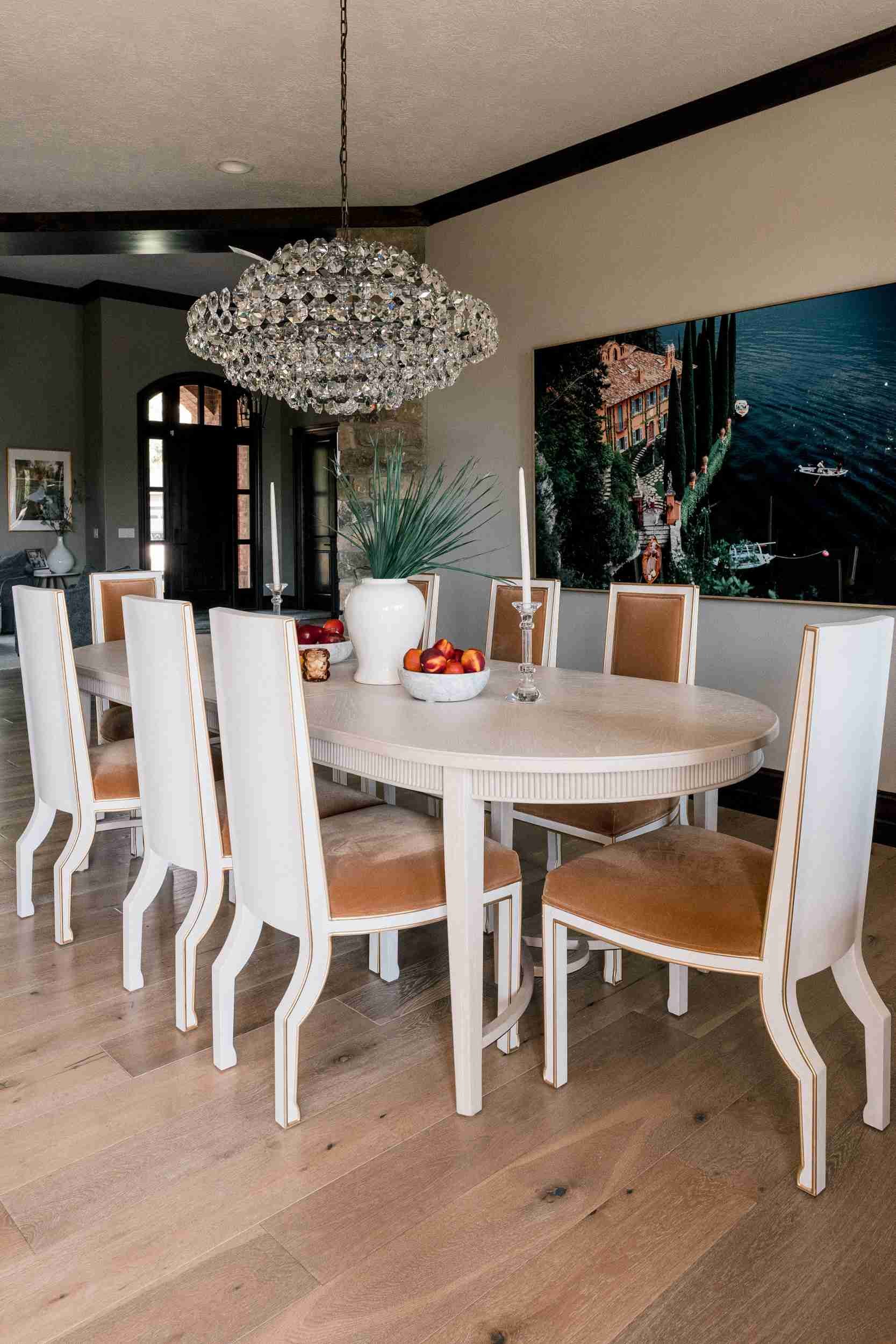 Long view of the elegant dining room with wood floors, high ceiling, white oval table, and a large scenic artwork on the wall.