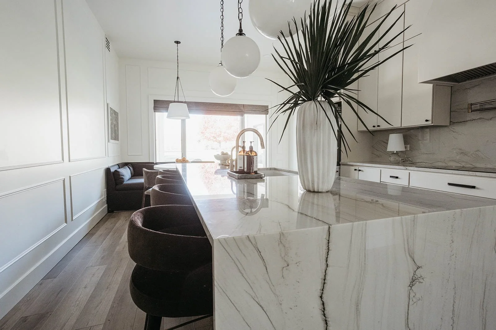 View of the spacious kitchen and dining area, highlighting the large marble waterfall island, dark stools, and a tall white vase with greenery.