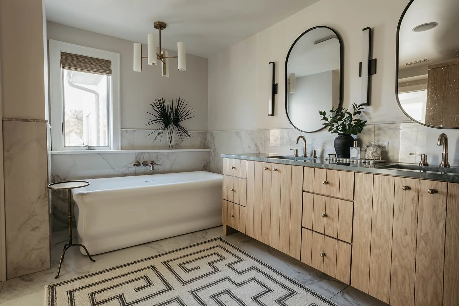 Bright, modern master bathroom featuring a natural wood double vanity, two arched mirrors, a freestanding bathtub, and a patterned tile inset on the floor.