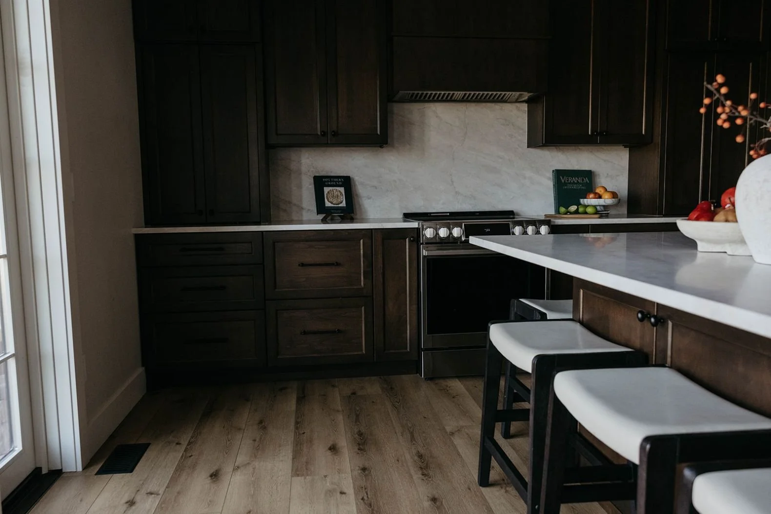 View of the kitchen showing the built-in dark wood cabinetry, the island with stools, and light wood flooring.