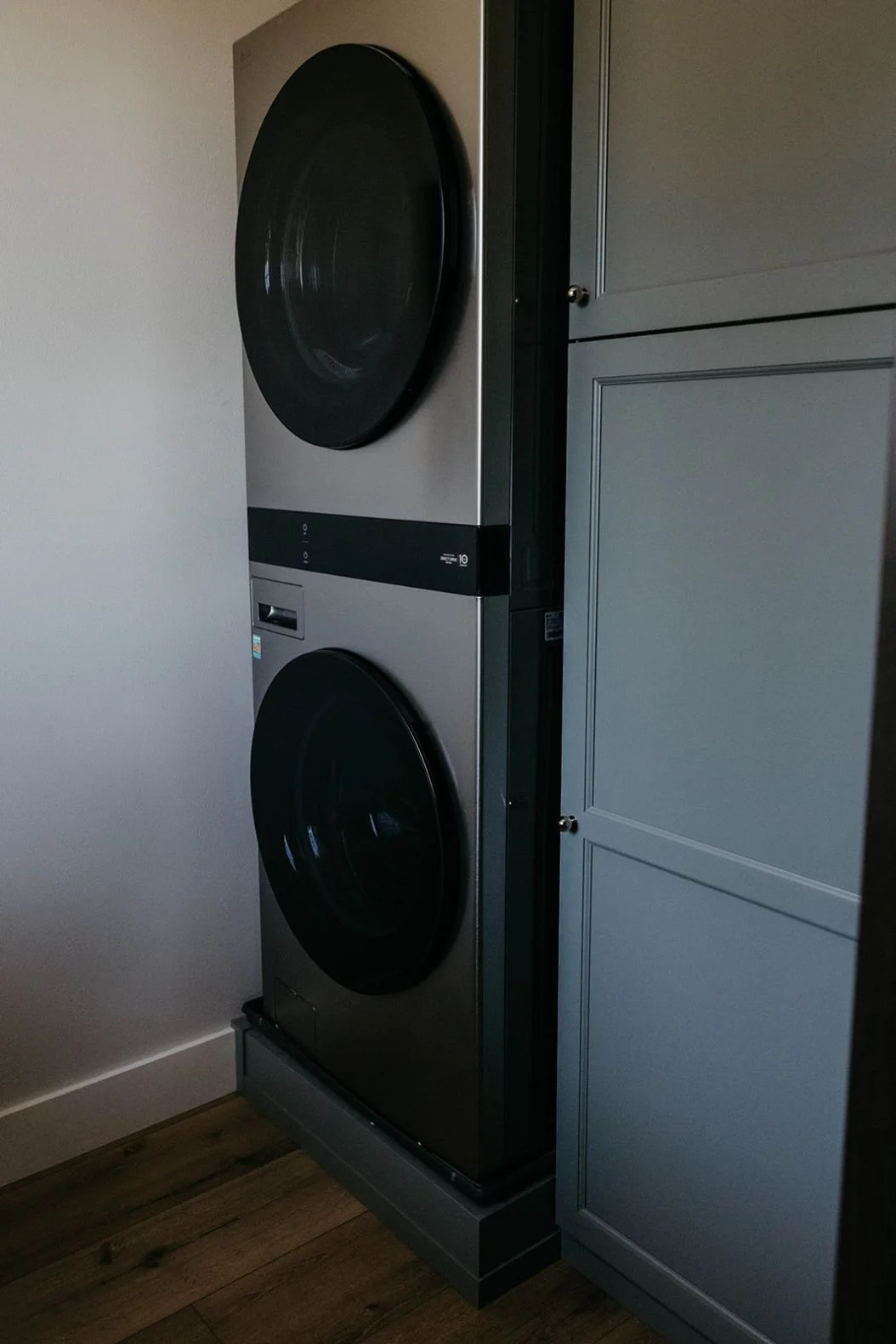 Stacked modern washer and dryer units, framed by floor-to-ceiling gray-green utility cabinets.