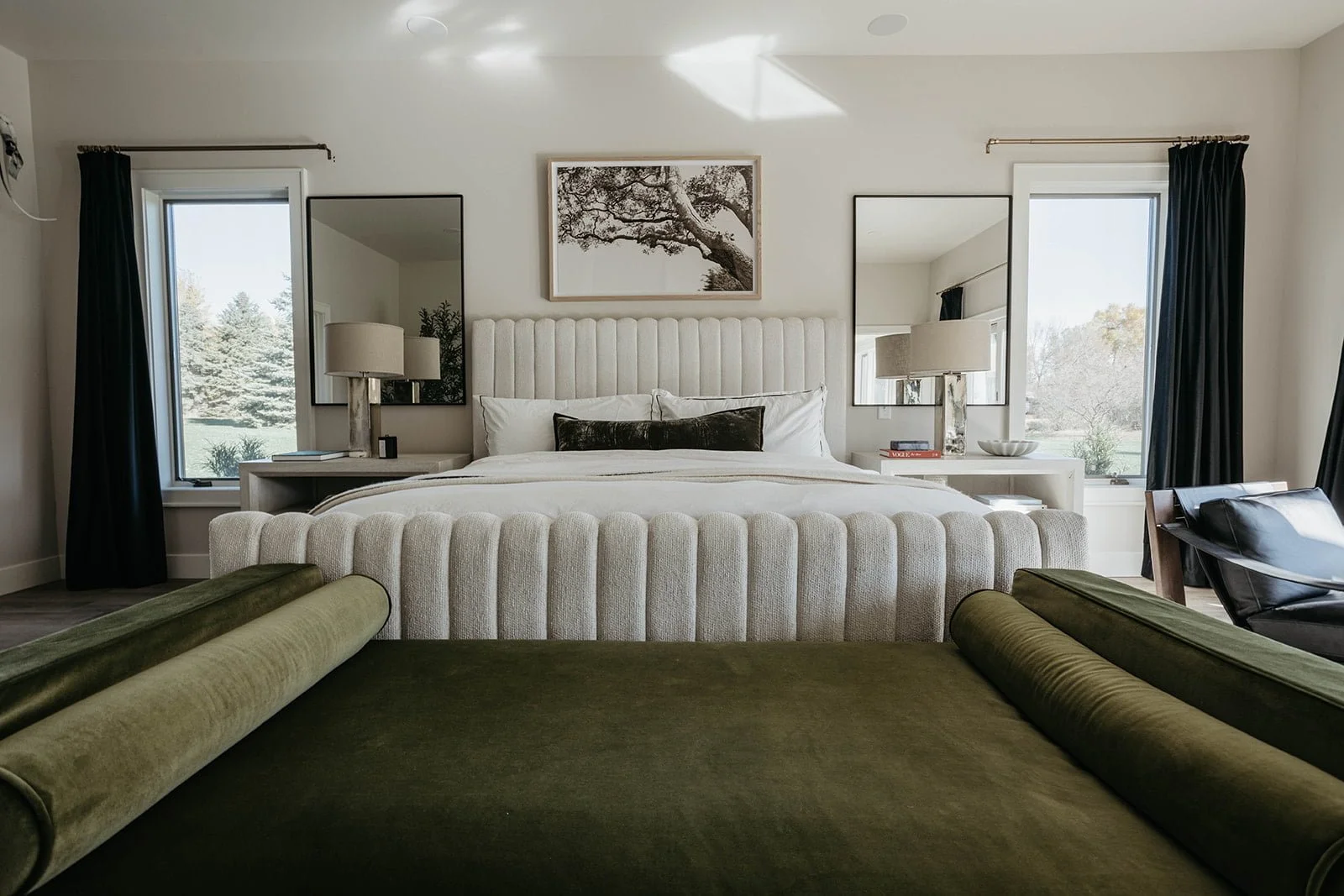 Luxurious master bedroom featuring a white channel-tufted headboard, a long olive green velvet bench at the foot of the bed, and mirrored nightstands.