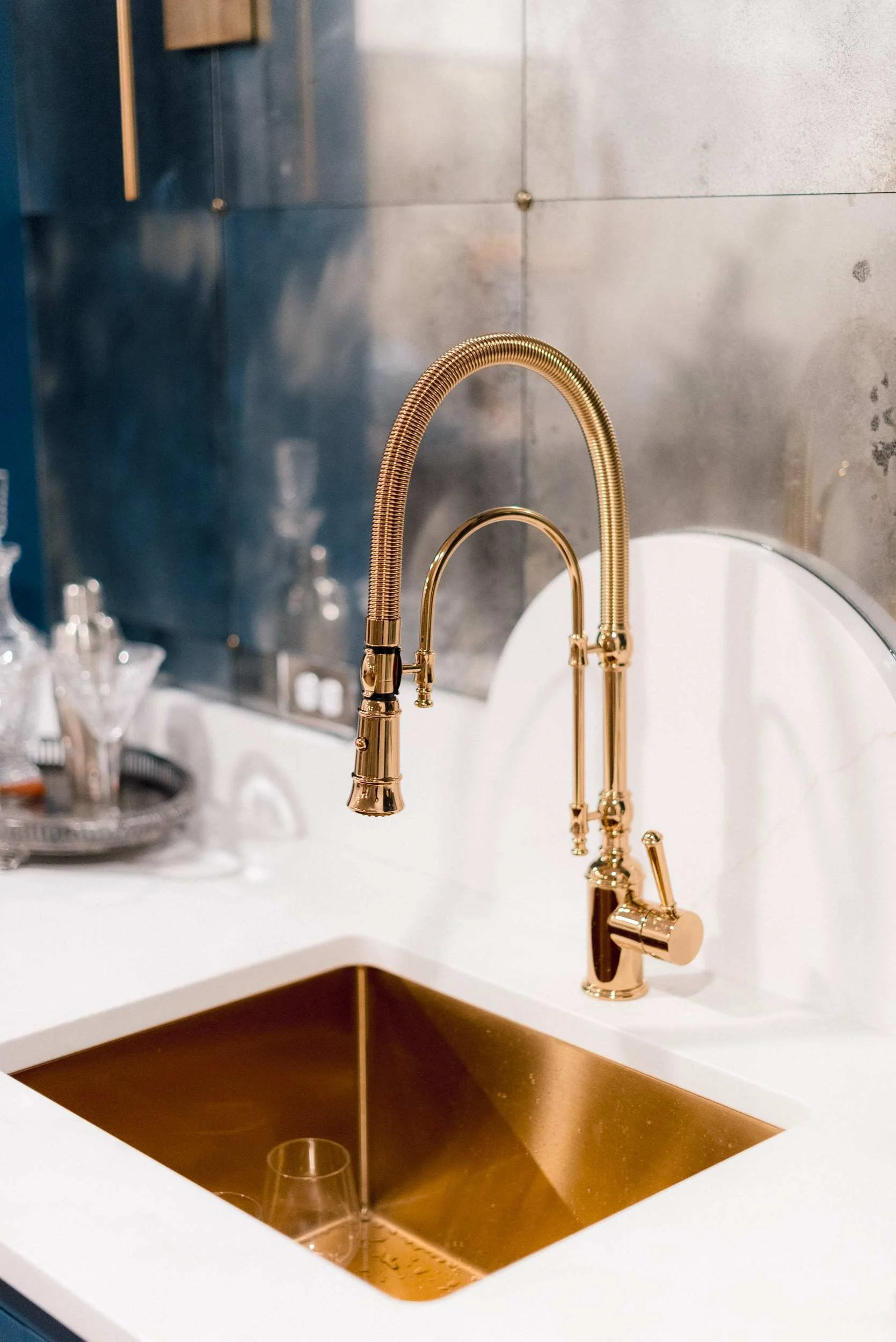 Extreme close-up of the brushed gold bar faucet arching over the square, gold-toned undermount sink, highlighting the white countertop.