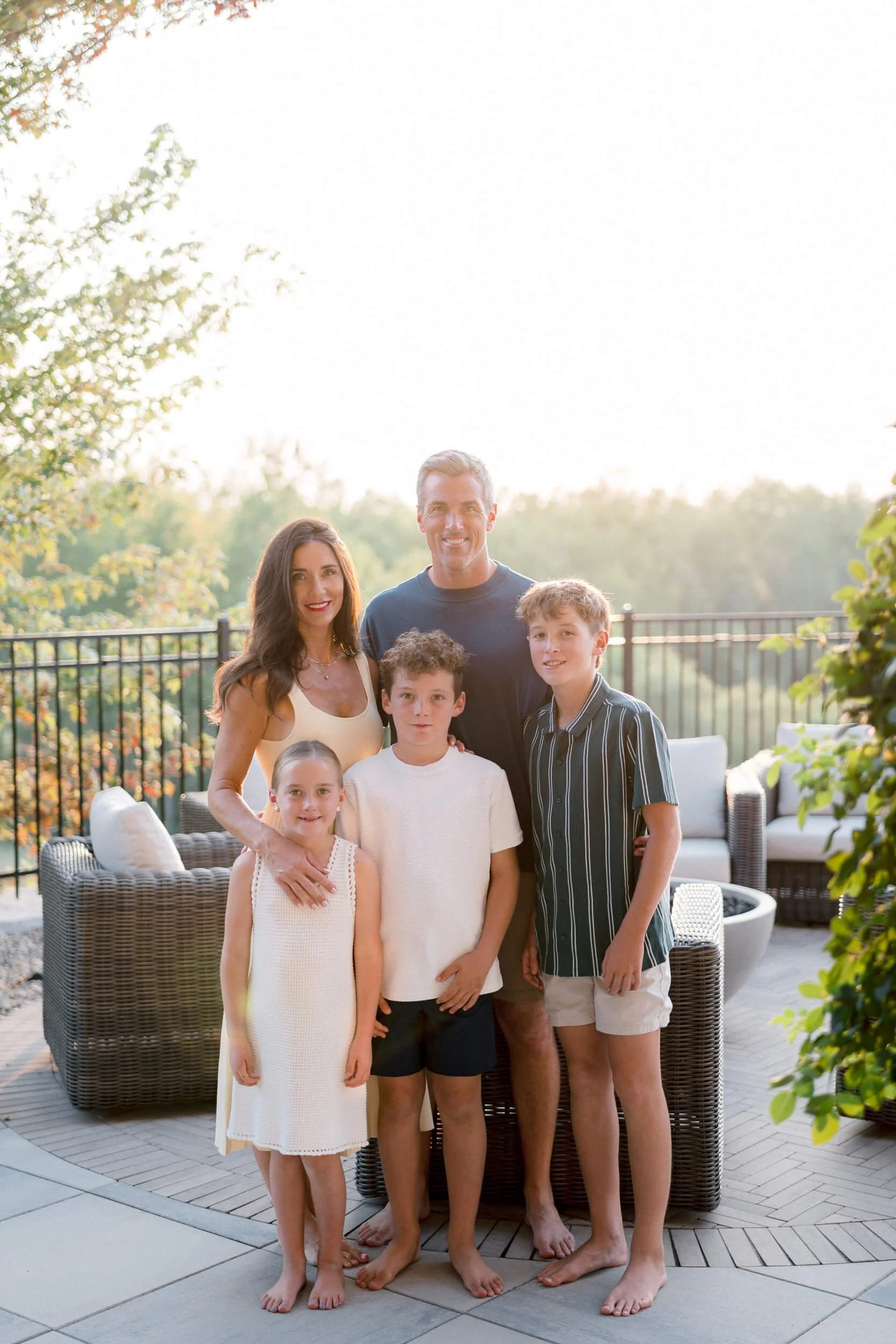 Christy Steen and her husband and three children posing outdoors on their poolside patio, under a tree, during sunset.