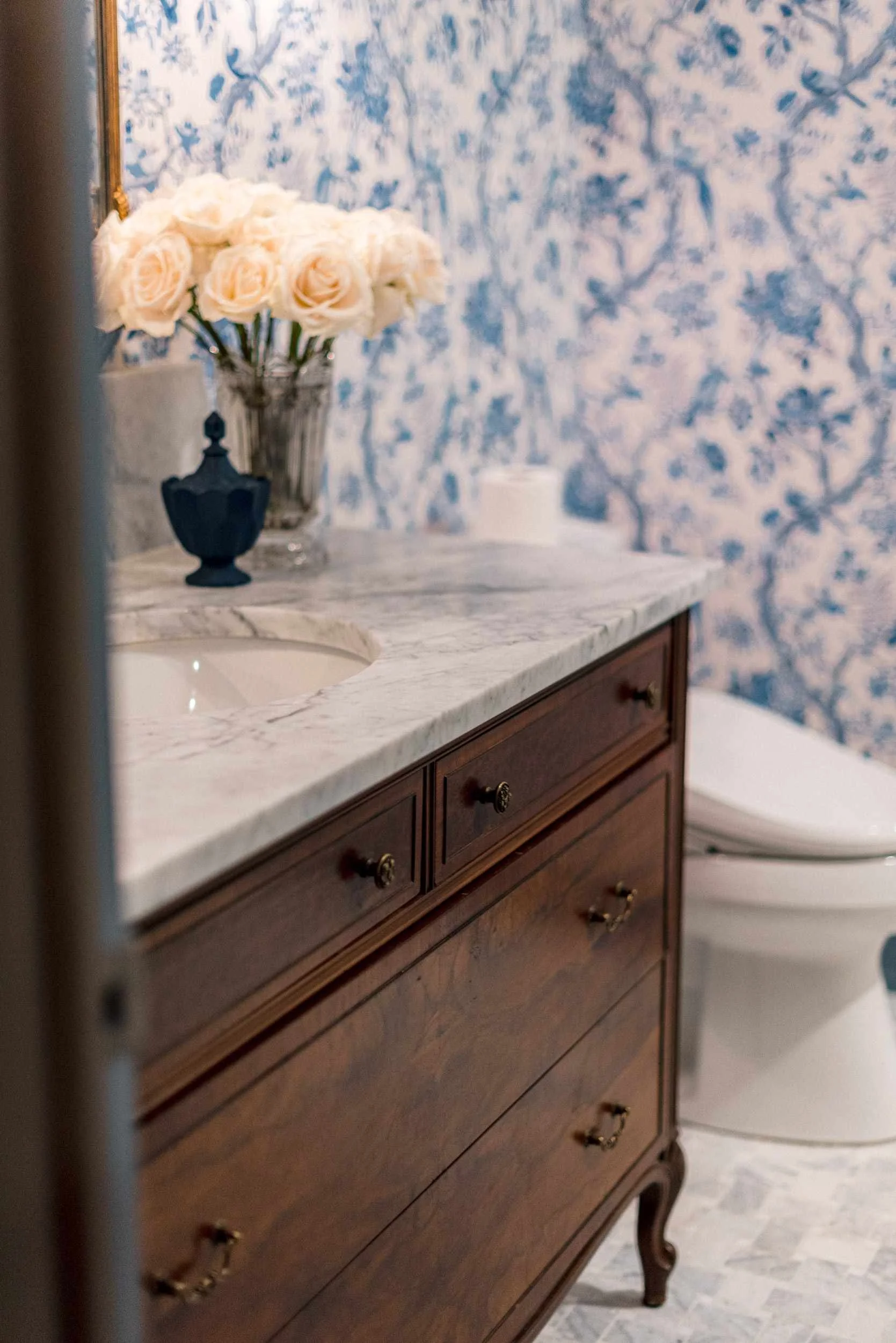 Side view of the dark wood vanity and marble top, showing the sink area and the white toilet visible in the reflection.