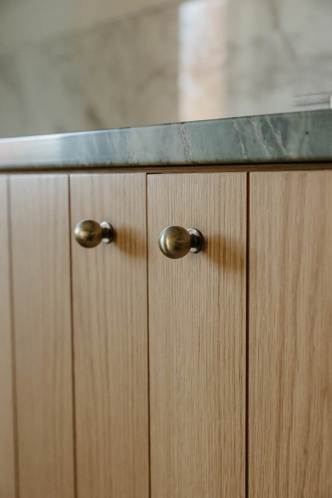 Detail shot of the natural wood vanity cabinetry with round brass knobs and a dark green countertop.