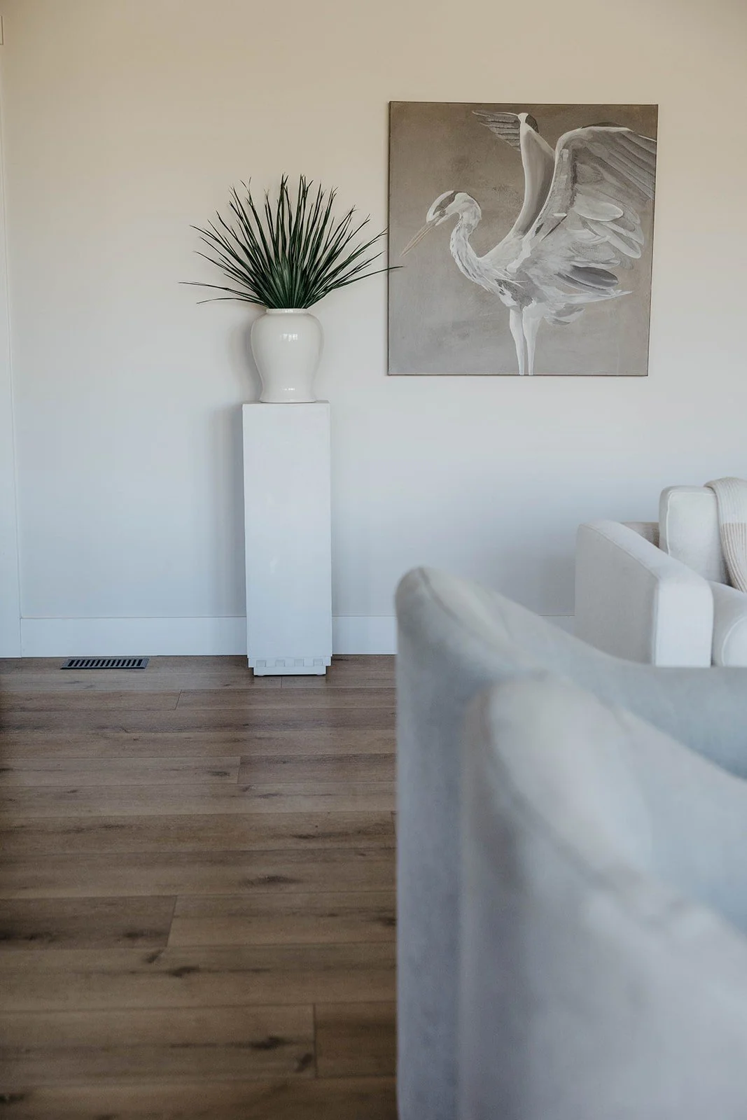 Neutral living room wall decor featuring a white pedestal with a plant and a large square heron or crane artwork.
