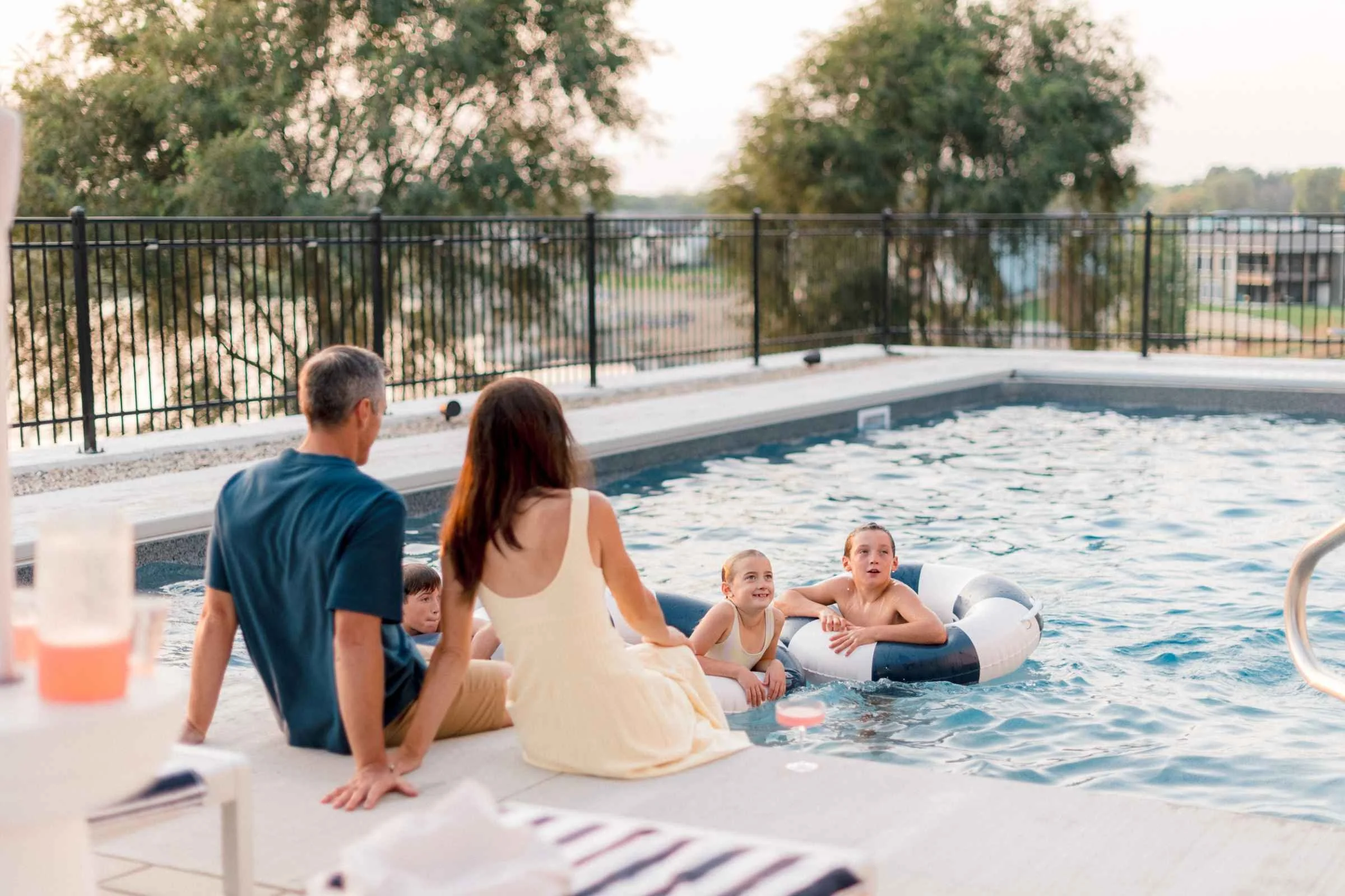 Family sitting on the pool ledge at water level, enjoying time together in the water.