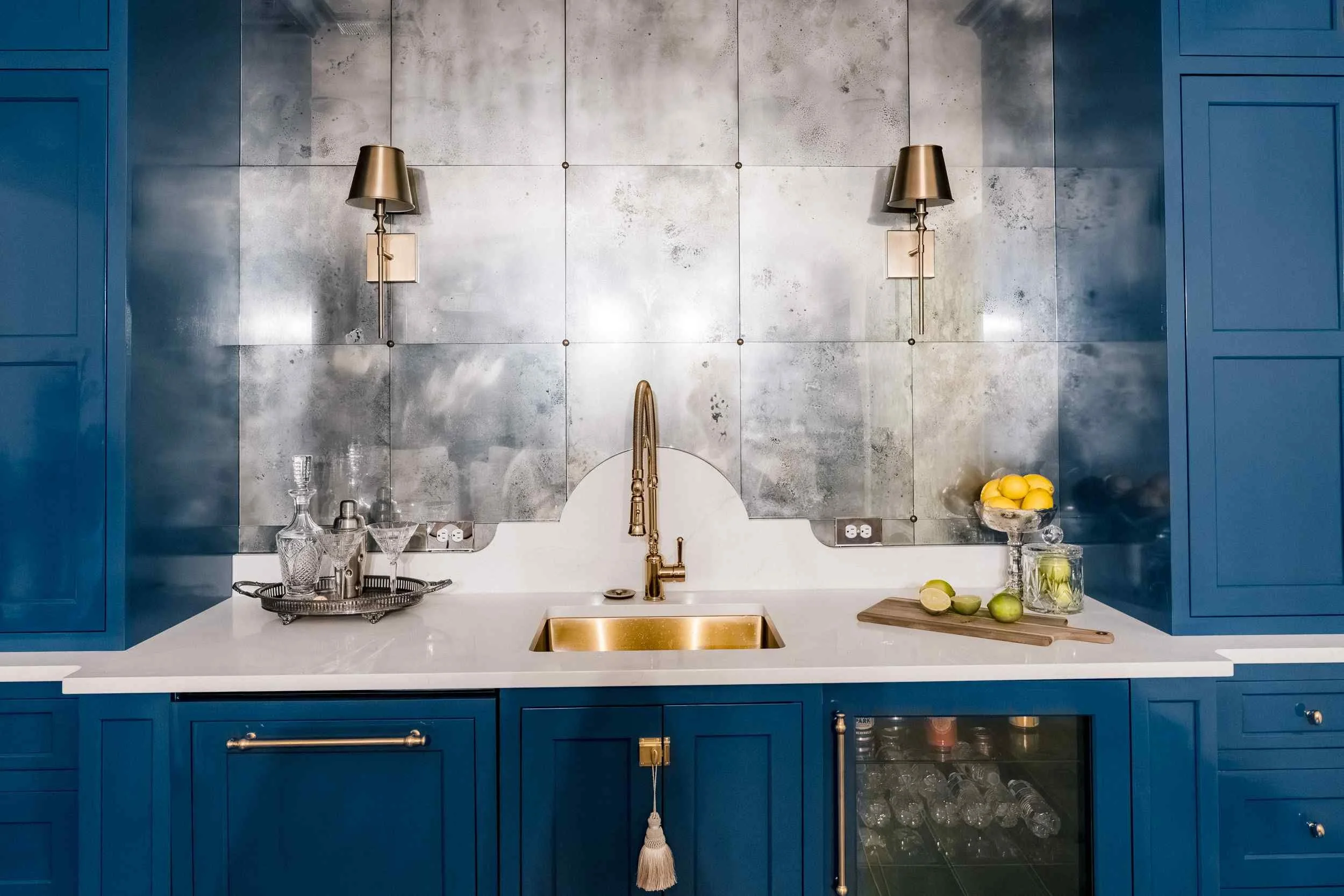 Close-up of the bar sink area, showing the gold curved faucet, white sink, and antique metal backsplash with gold wall sconces.