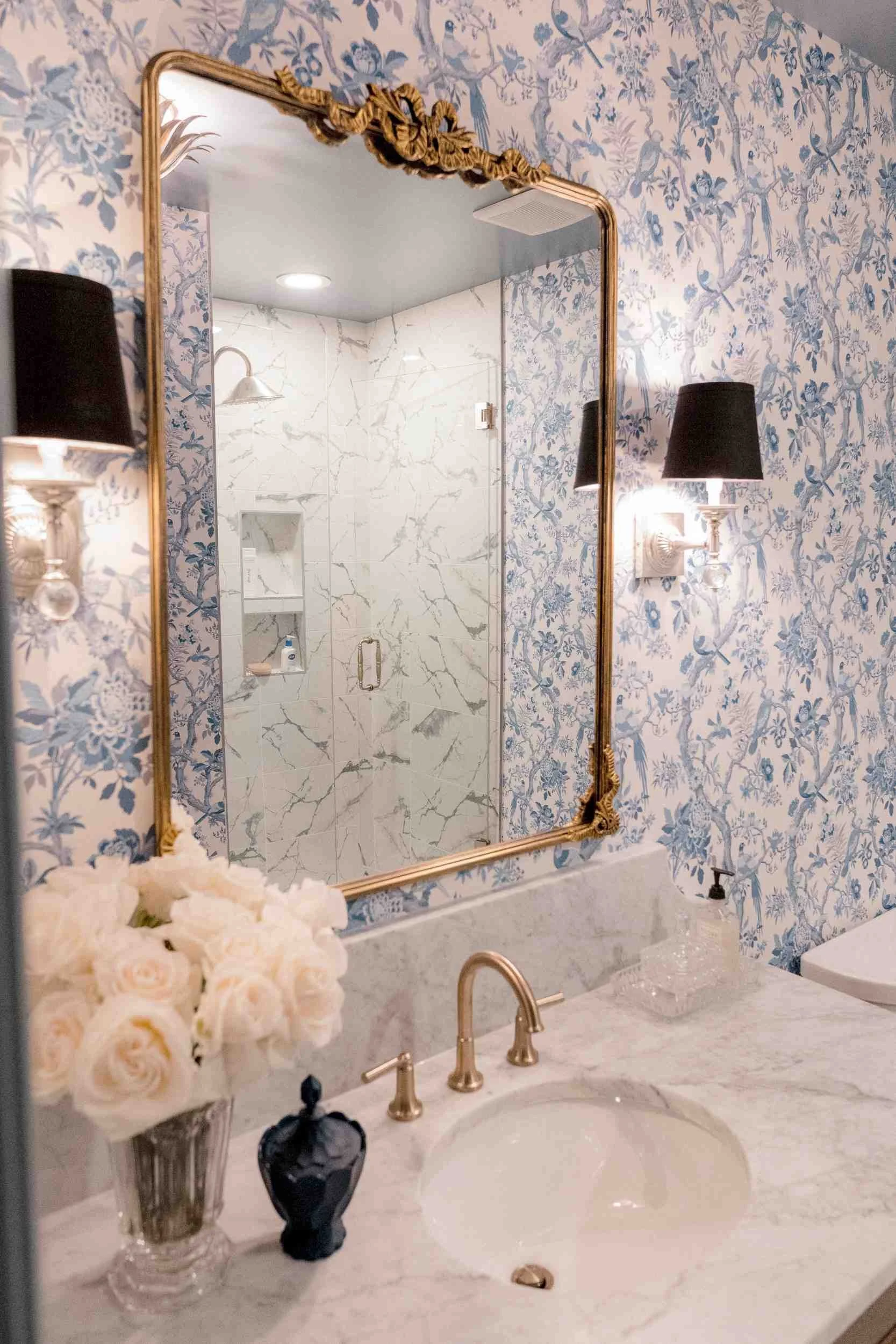 Full view of the powder room vanity, showcasing the large ornate gilt mirror, the marble countertop, and the blue and white toile wallpaper.