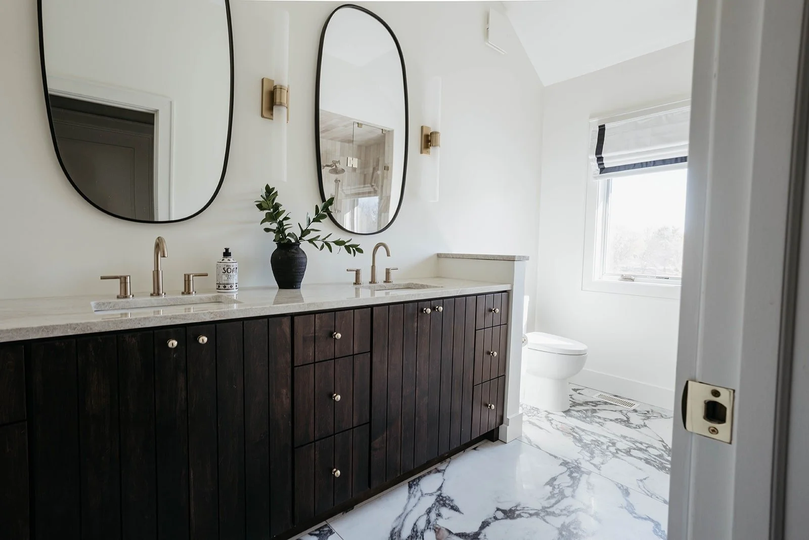 Elegant secondary bathroom with a dark wood double vanity, white marble floor, and two oval black framed mirrors above the sink area.