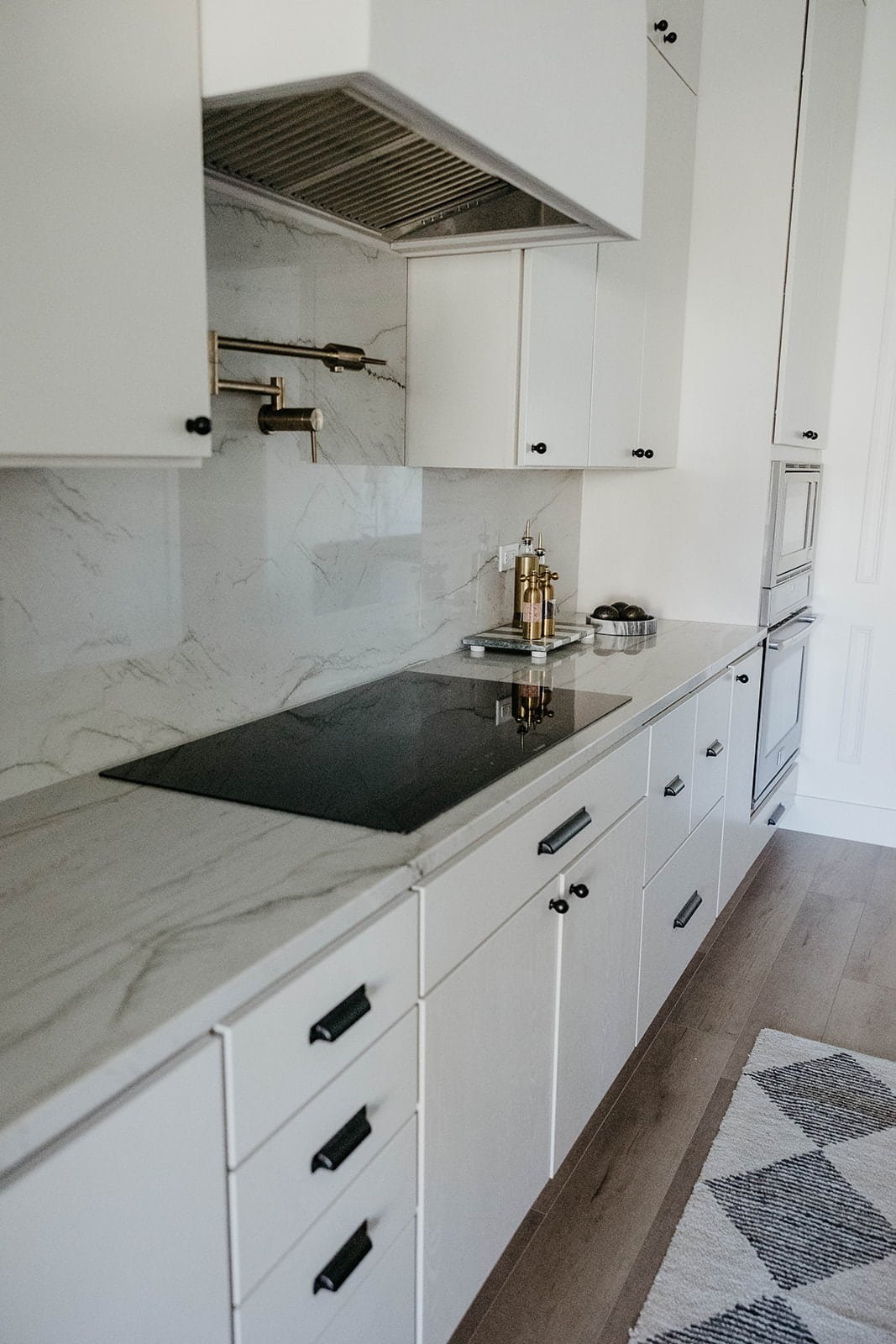 Full view of the bright kitchen cooktop area, featuring white shaker-style cabinetry, black pulls, and a white marble slab backsplash with gray veining.