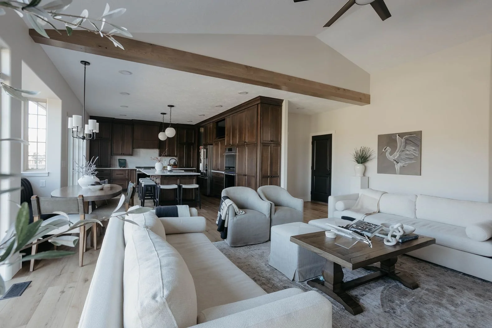 Wide, open-concept living space with high ceilings, exposed wood beams, and a view of the adjacent dining and kitchen areas.