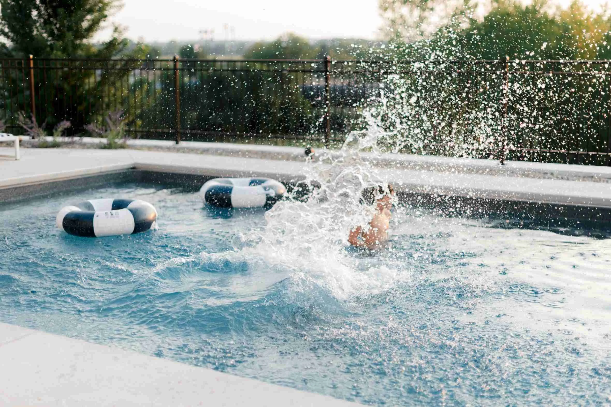 Child making a big splash while playing in the pool, surrounded by navy and white striped ring floats.