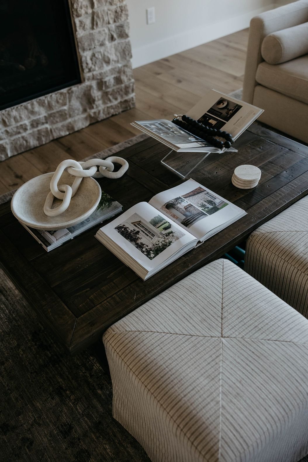 Close-up of the dark wood coffee table styled with open books and a square, textured ottoman pushed against it.