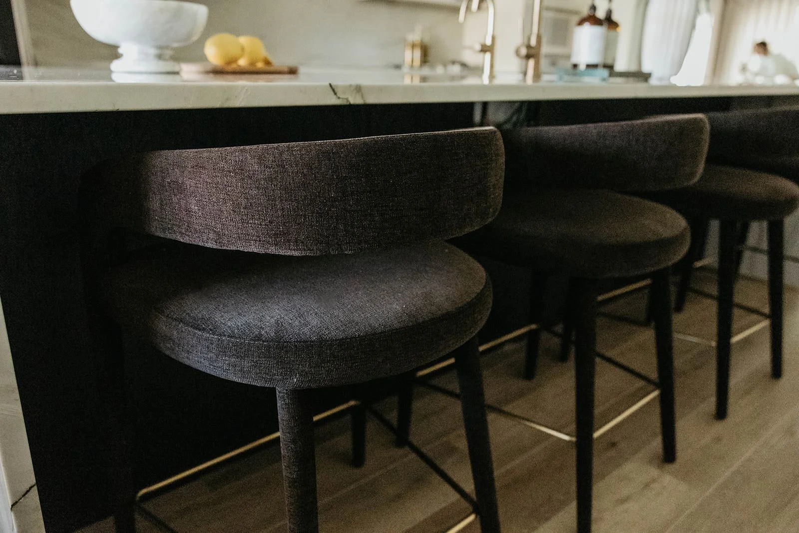 Close-up of two dark, textured counter stools with brass accents at the black-base section of the large kitchen island.