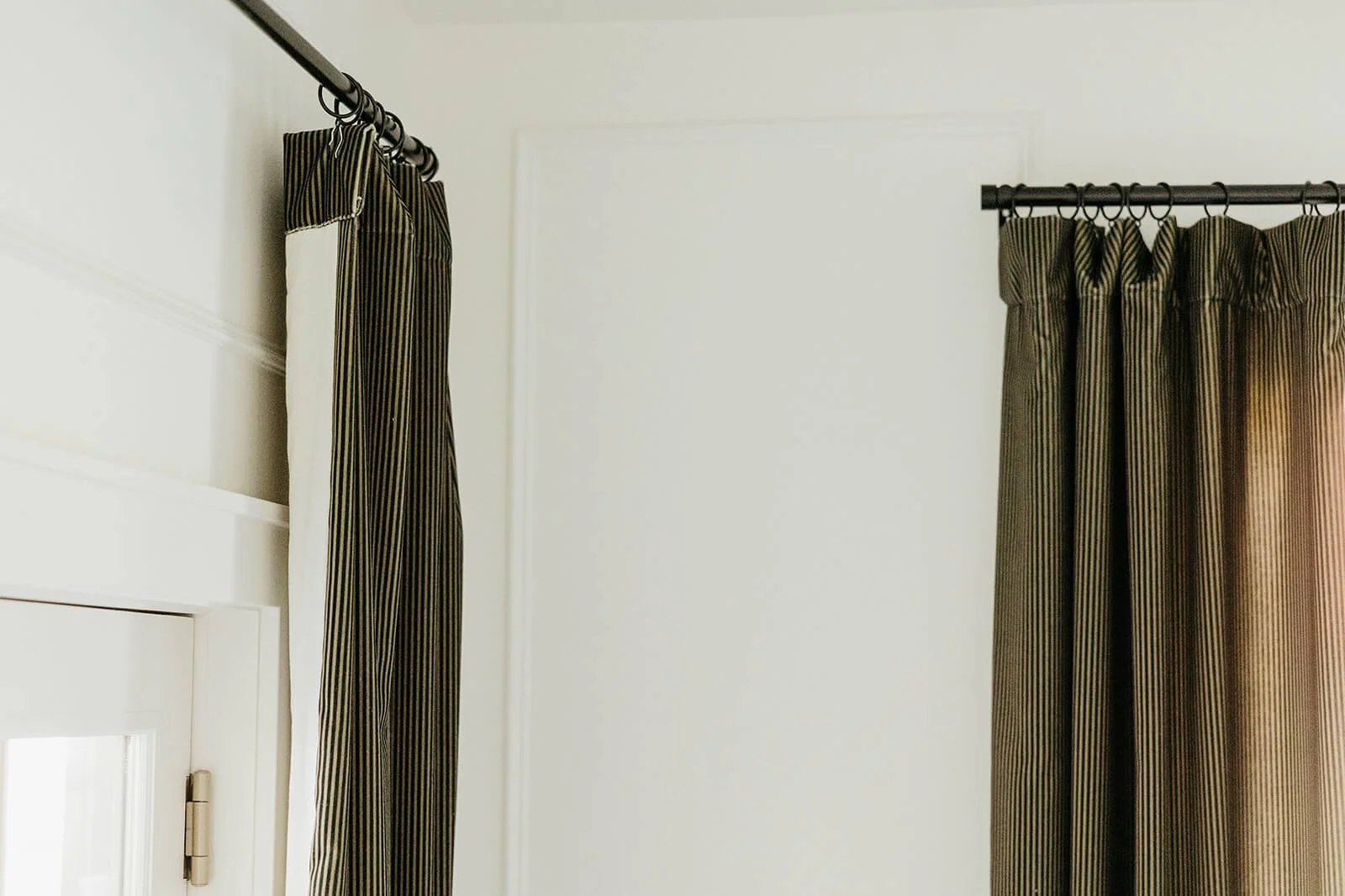 Close-up of a dramatic, dark bronze-colored velvet curtain and rod against a simple white wall and trim.