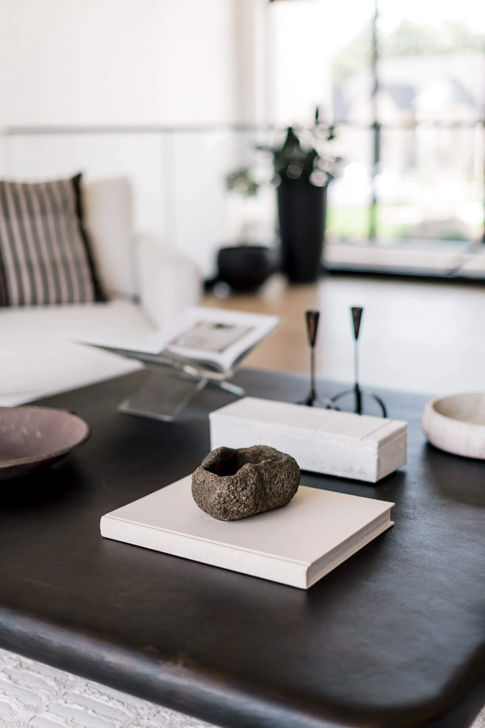 Detail shot of the modern dark wood coffee table, styled with decorative white books, black candlesticks, and a small sculptural rock.