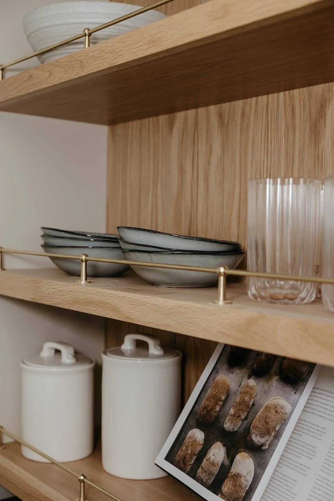 Close-up of the custom wood shelving in the coffee bar, showing plates and bowls stacked, with brass guard rails and large white canisters below.