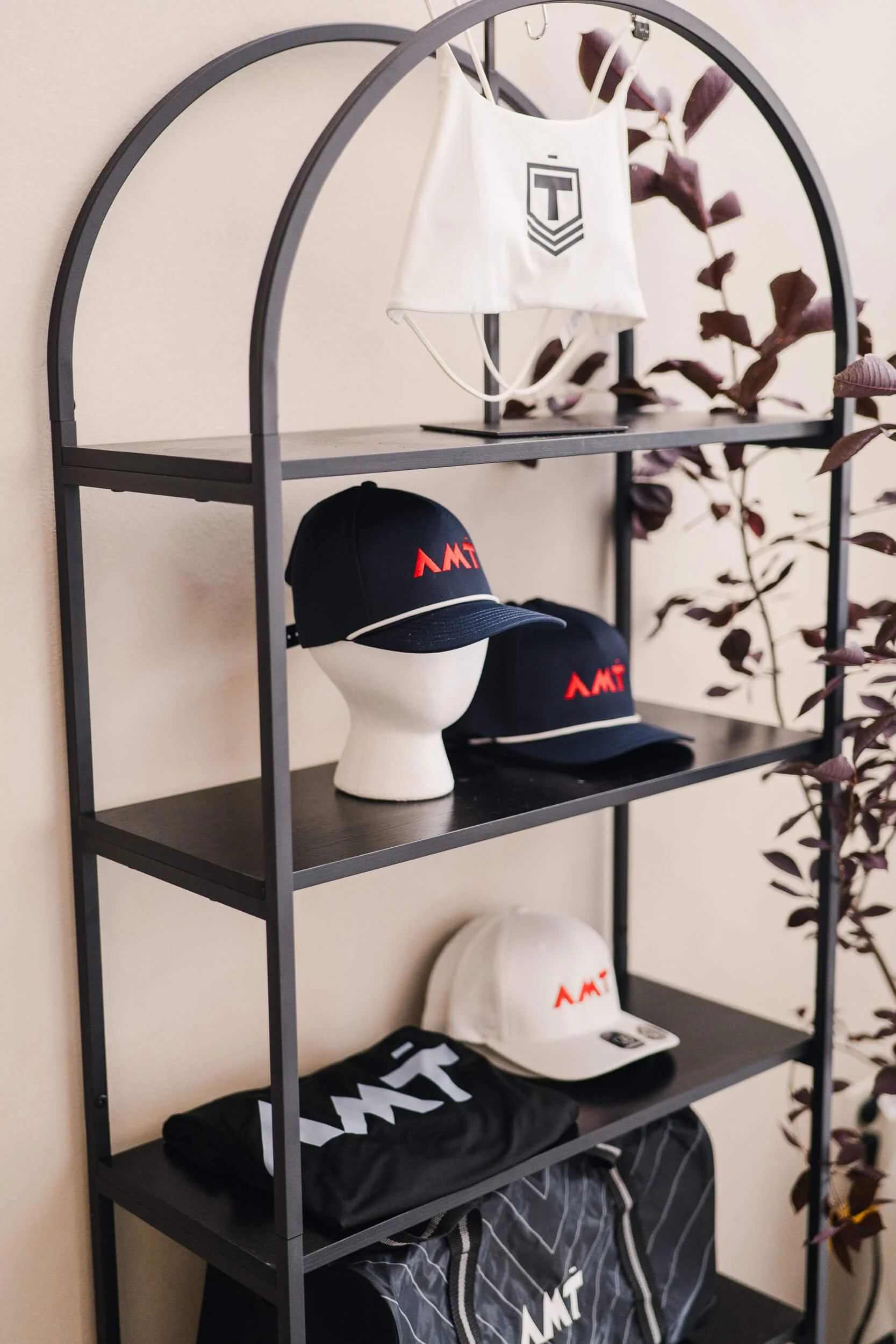 Close-up of the black arched metal shelf showing the hats and apparel with the business's branding.
