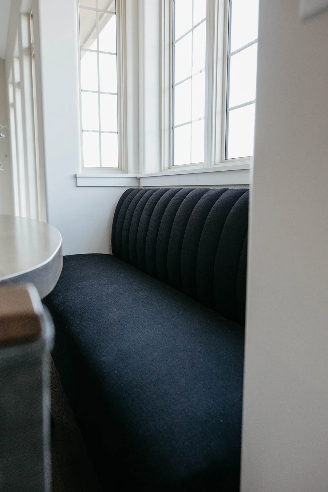 Detail of a black velvet channel-tufted banquette built into a sunny window nook.