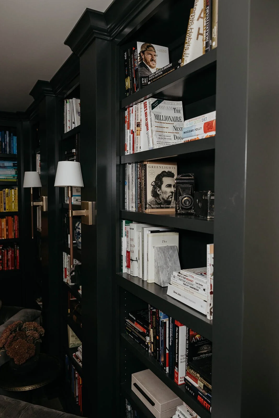 Close-up of dark green built-in bookshelves styled with books, a framed portrait, and a vintage camera, showing a glimpse of the crown molding.