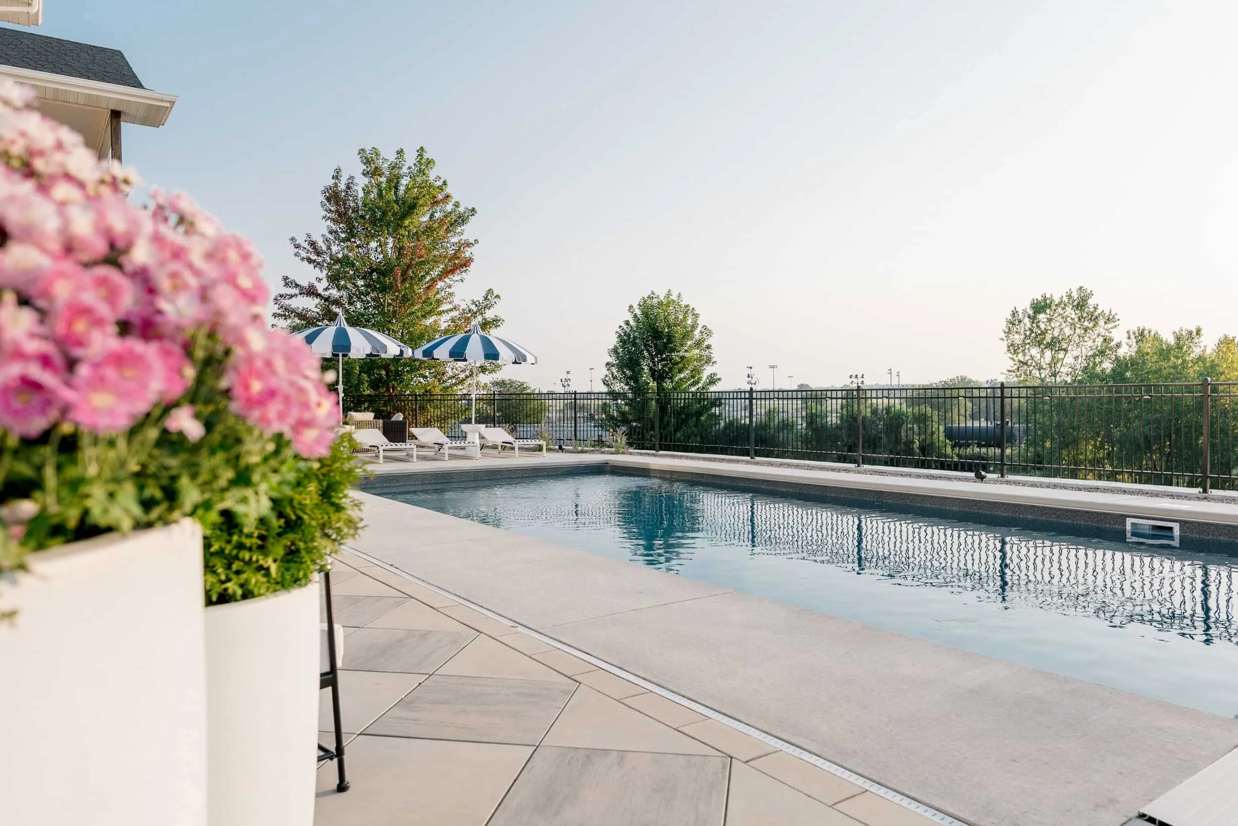 Rectangular in-ground pool on a concrete patio, framed by a large white planter of pink hydrangeas in the foreground.