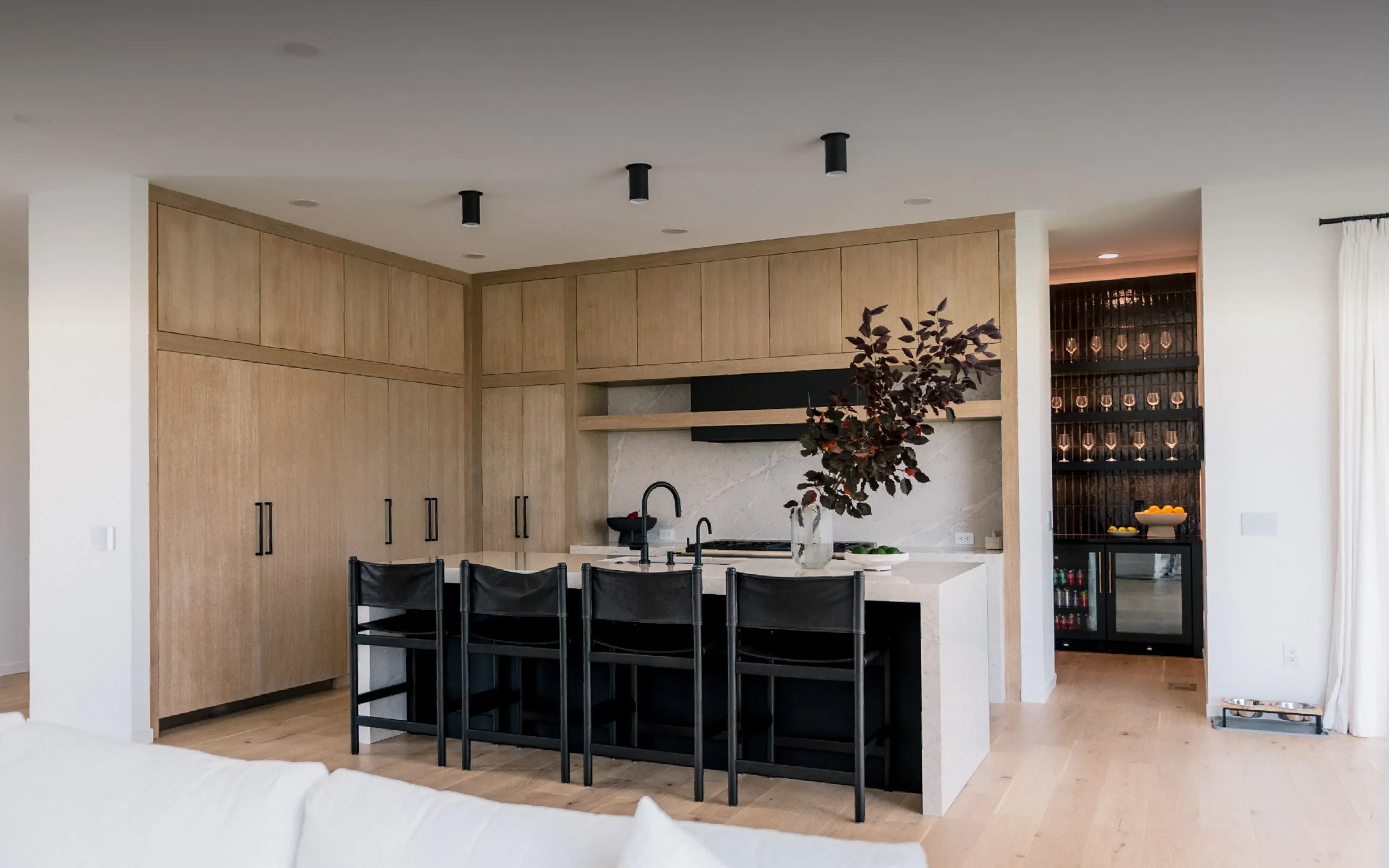 Modern open-concept living room and kitchen with white sofa, black chairs, wooden flooring, and minimalist decor.