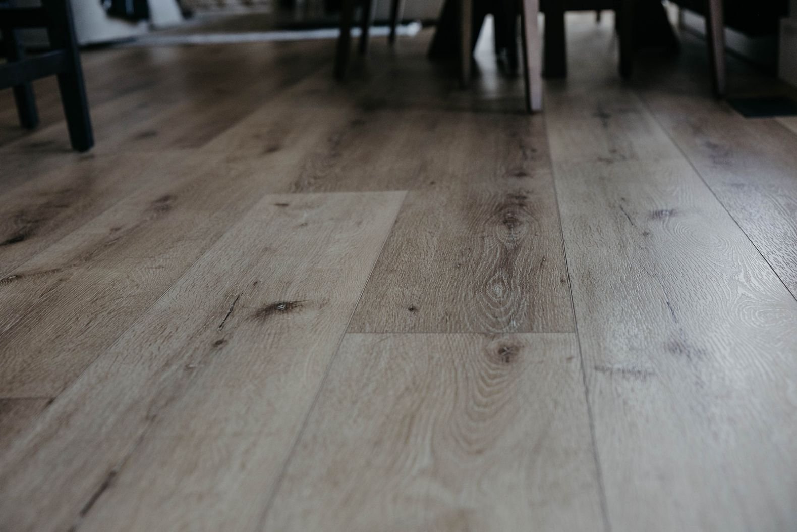 Close-up of the light, textured wood plank flooring in a sunlit area, showing the variation in the wood grain.